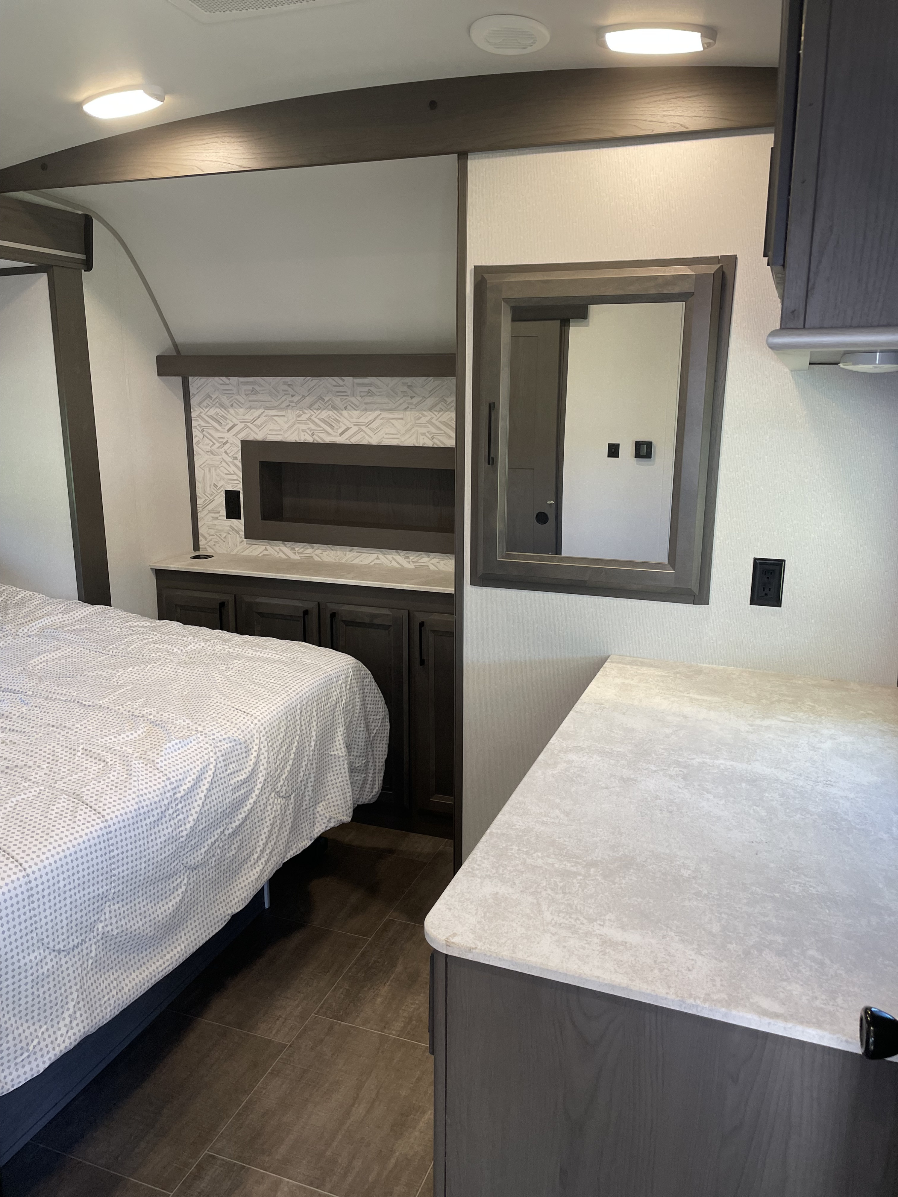 Modern RV rental bedroom with a comfy bed, dark wood cabinetry, light countertops, and a large mirror. Tiled floors.. Cruiser Rv Corp Stryker 2021