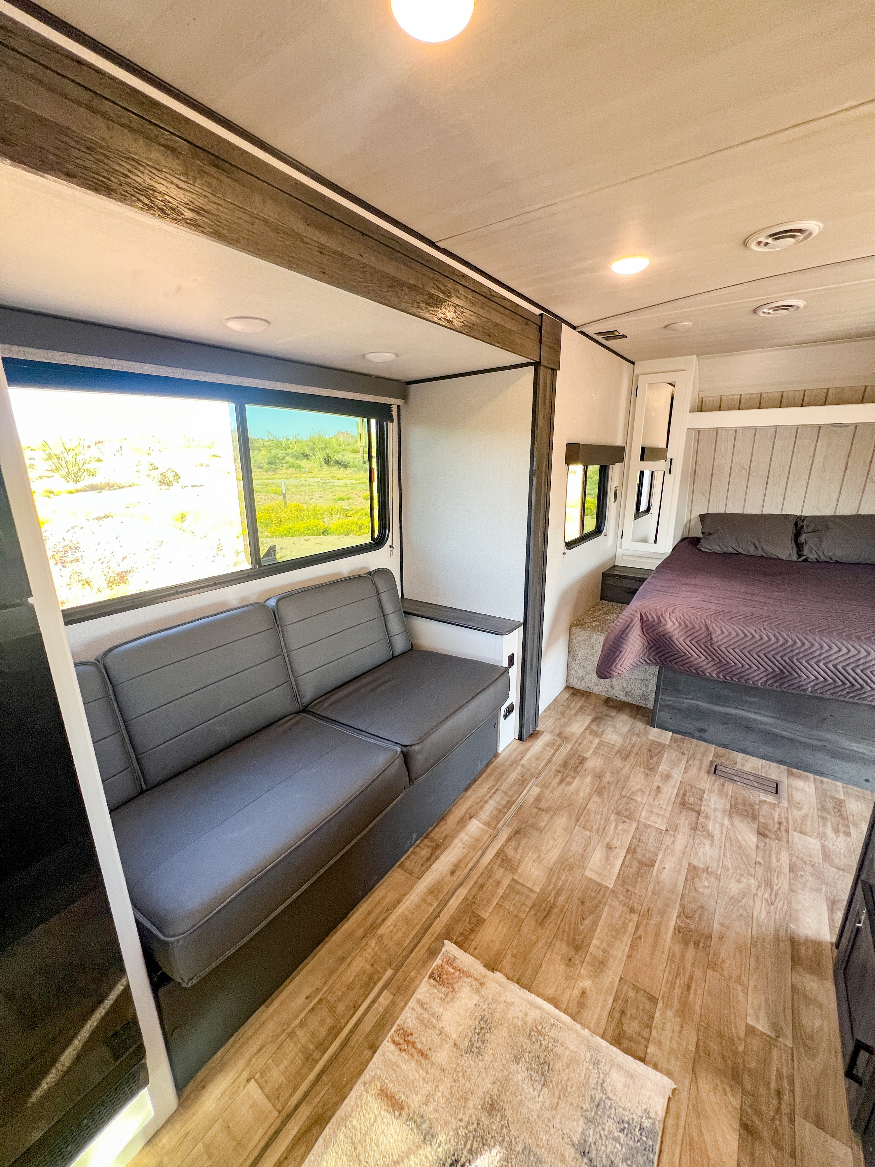 Modern RV rental interior with bright windows, a gray sofa, and a separate bedroom.. Keystone RV Hideout 2023