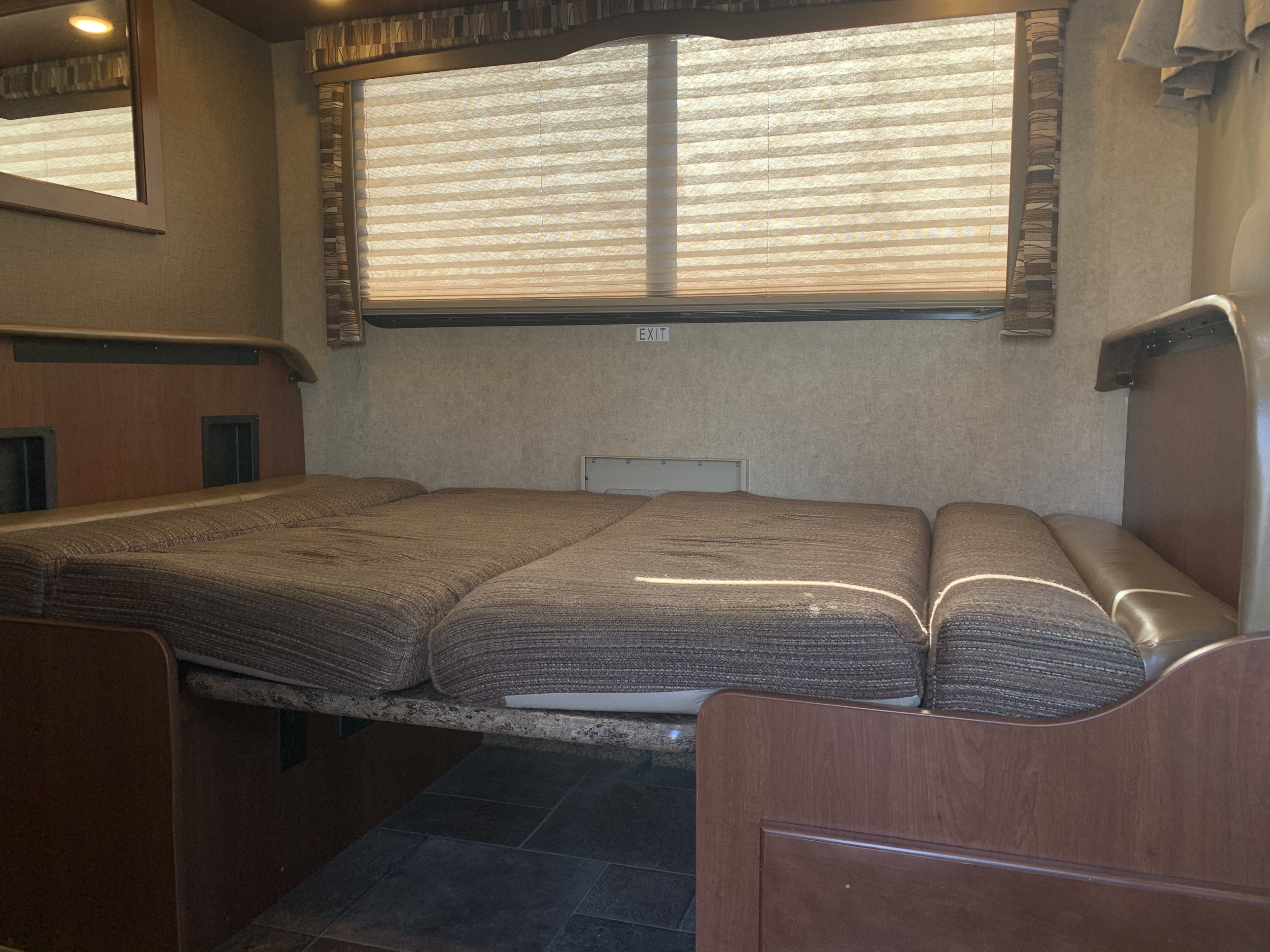 Comfortable RV rental interior with a cozy bed setup, window blinds, and wood accents. Perfect for travel.. Thor Motor Coach Chateau 2017