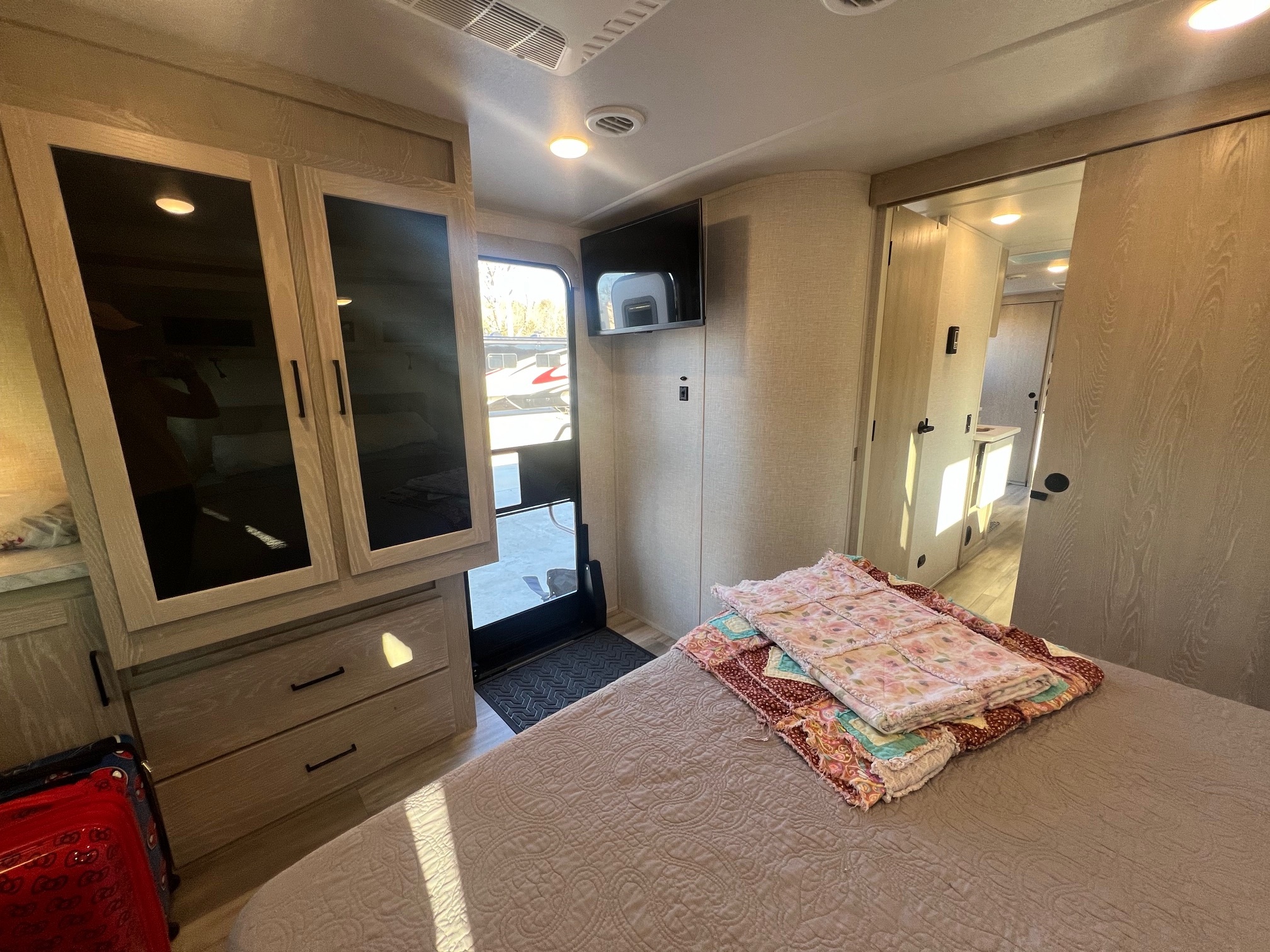 RV rental bedroom: A textured bed with quilts, mounted TV, wooden dresser, and open door offering an outside view.. Forest River Rockwood Ultra Lite 2023