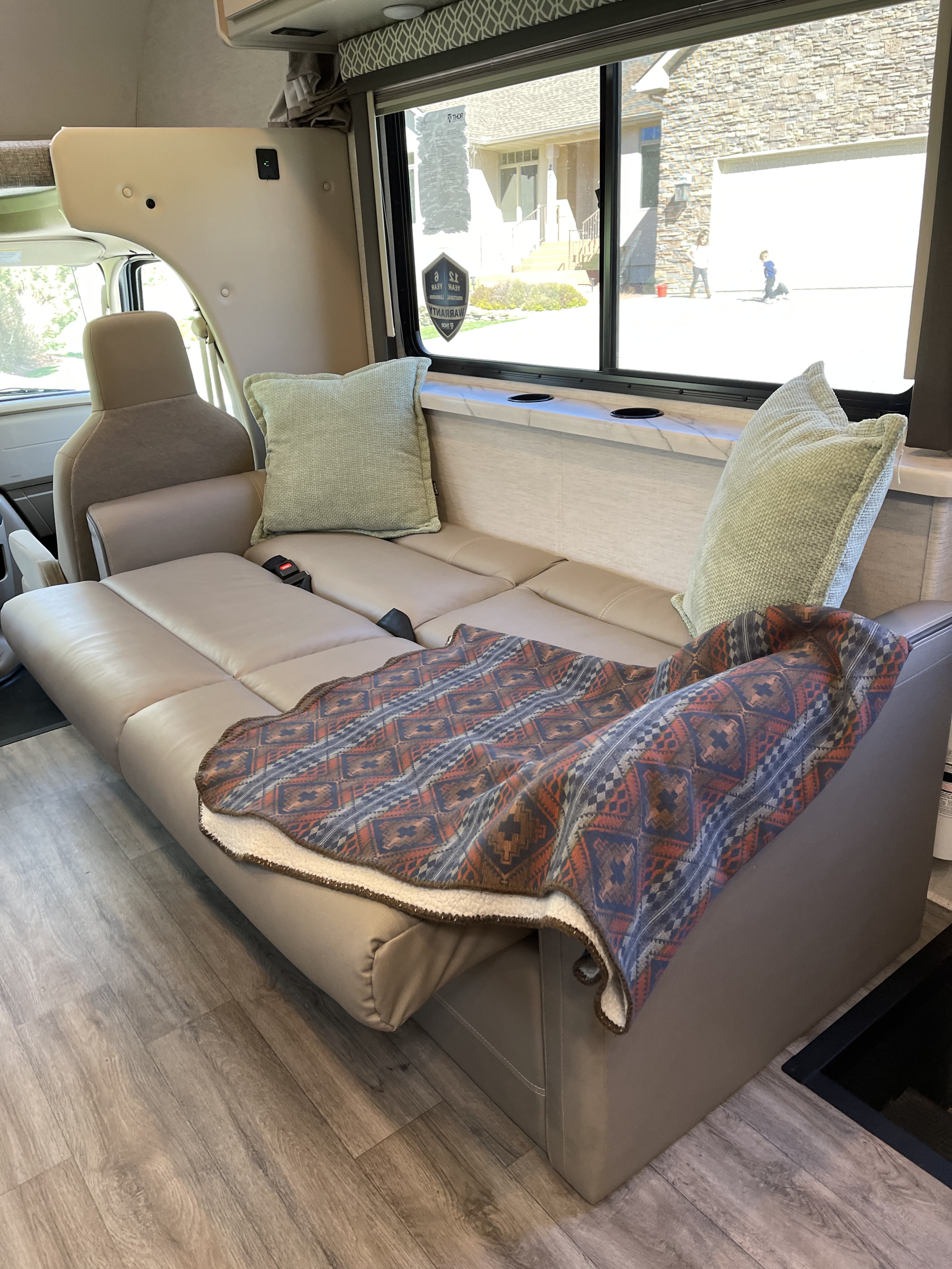 Cozy RV rental interior with a spacious, tan sofa that converts to a bed, adorned with pillows and a patterned blanket.. Thor Coleman 2024