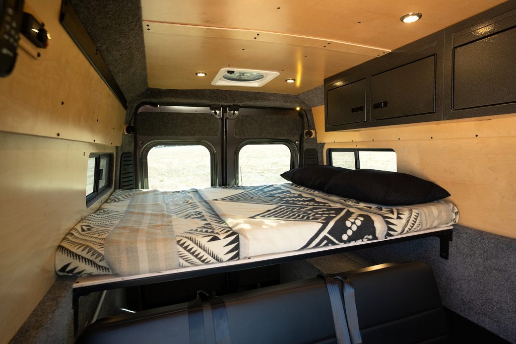 Spacious camper van interior with elevated bed, cozy bedding, overhead storage & rear windows, ideal for RV rental.. Dodge RAM Promaster 159" 2023
