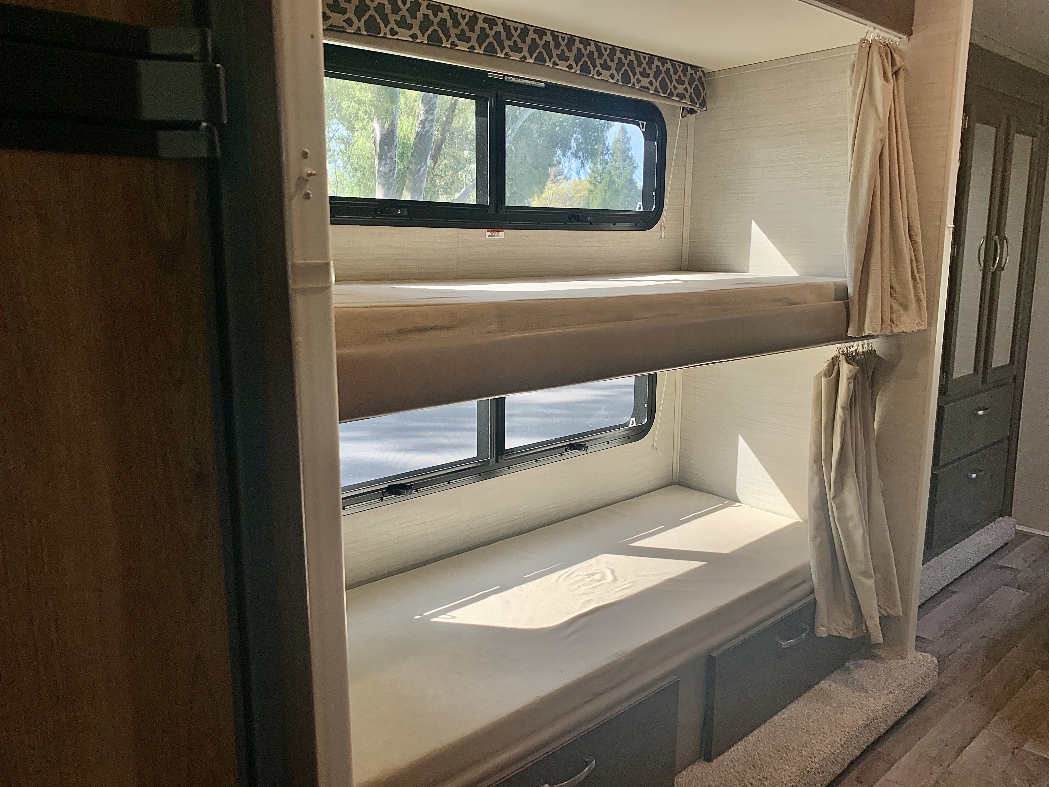 RV rental: Interior view of stacked bunk beds with windows showing trees, curtains, and built-in storage.. Jayco Redhawk 2019