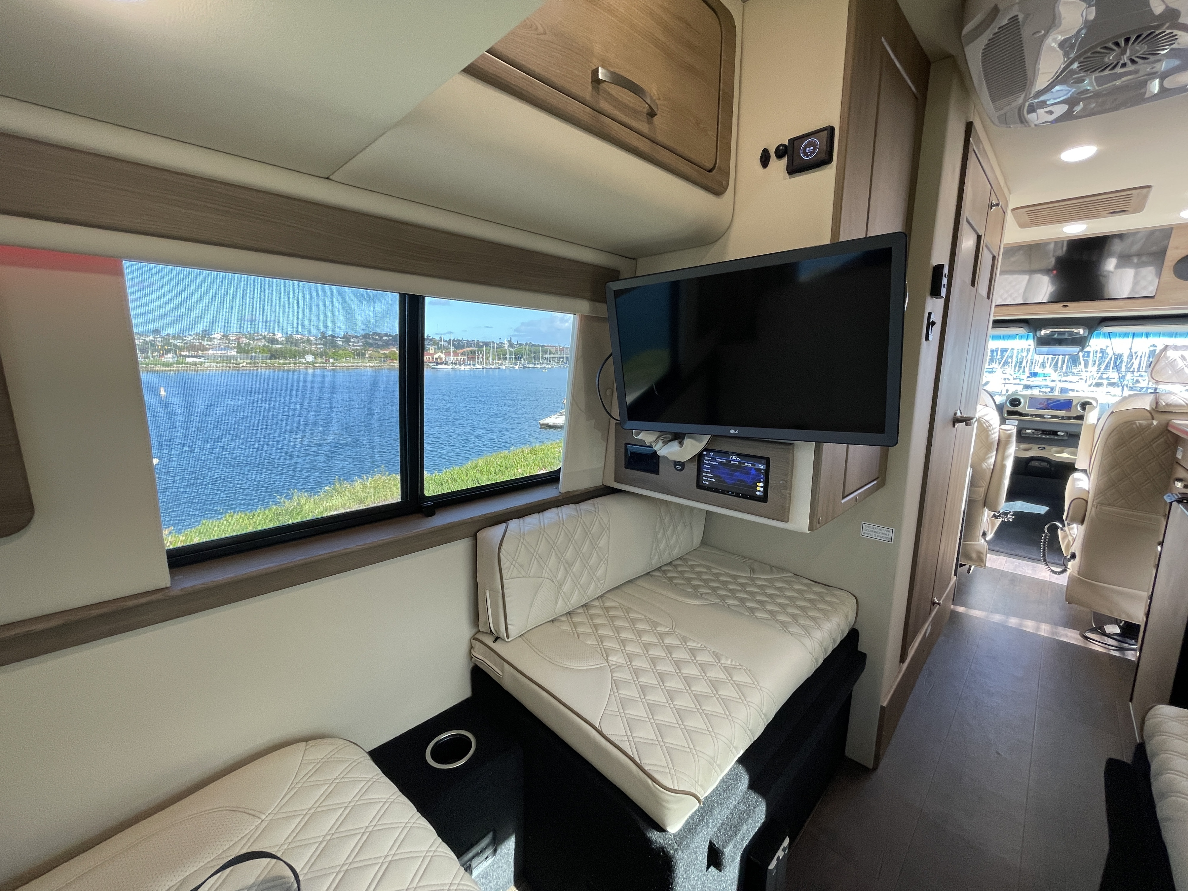 Spacious RV rental interior with panoramic window views of a marina. Plush seating and entertainment for comfortable travel.. Mercedes-Benz Sprinter 2023