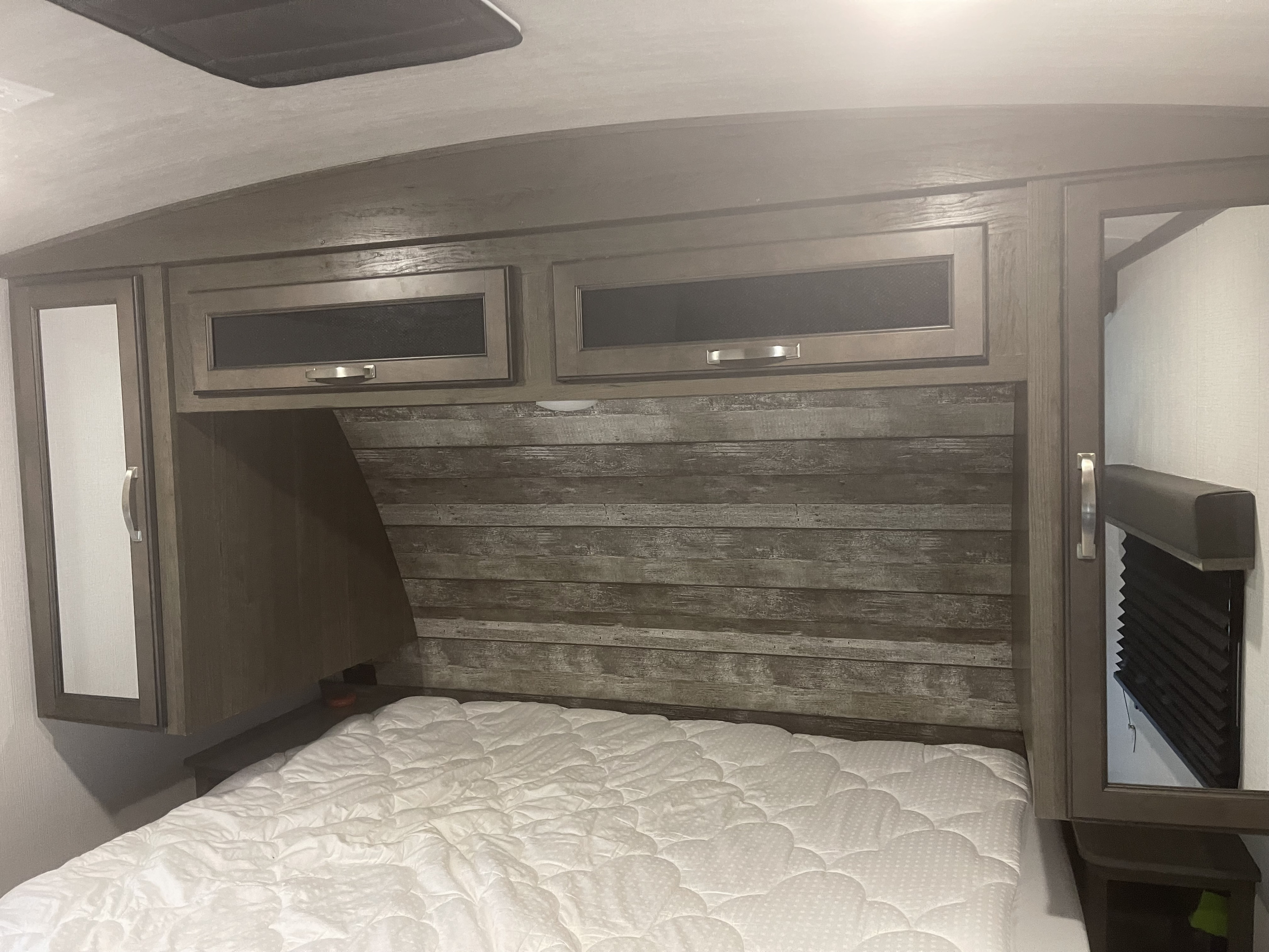 RV rental bedroom: Compact sleeping area with overhead storage, wood-panel headboard, and white quilted mattress.. Keystone RV Cougar 2021