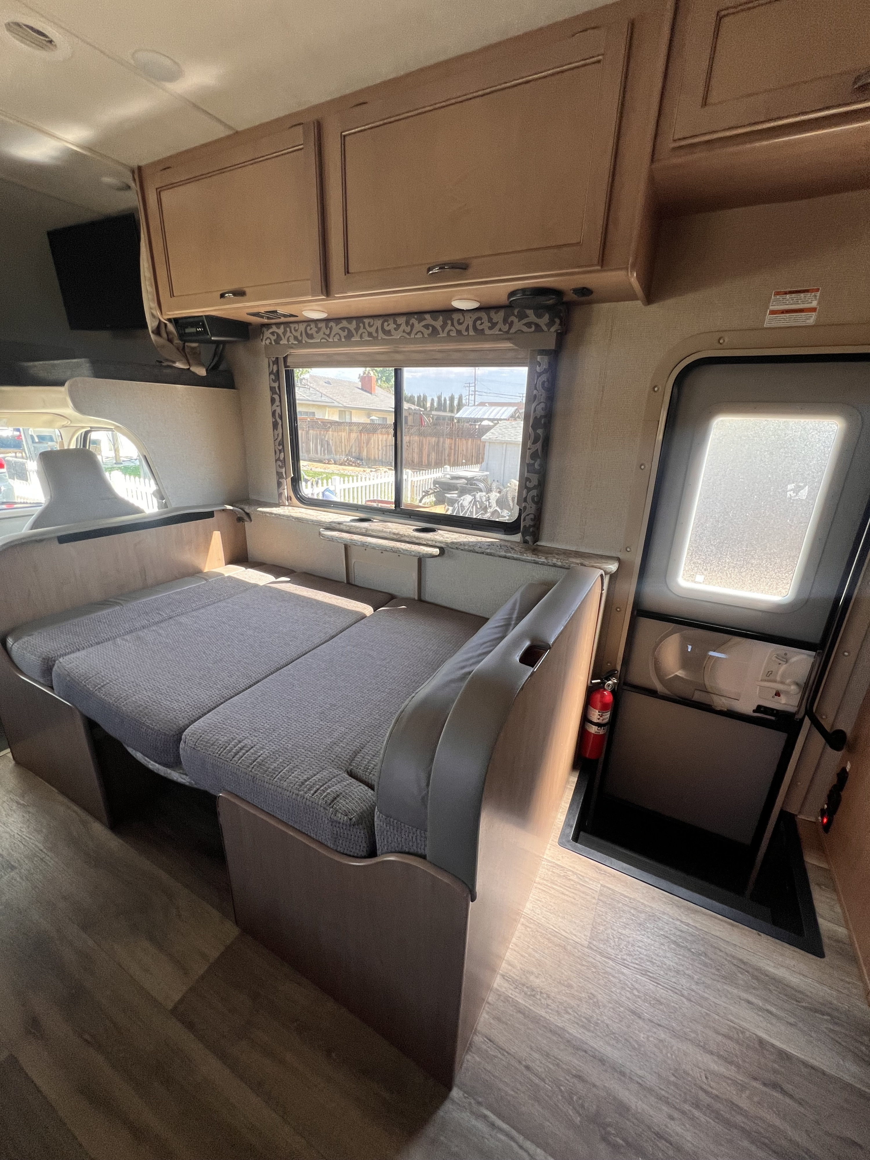 RV rental interior: Dinette converts to a bed, with overhead cabinets, a view from the window, and an entry door.. Thor Four Winds 2019