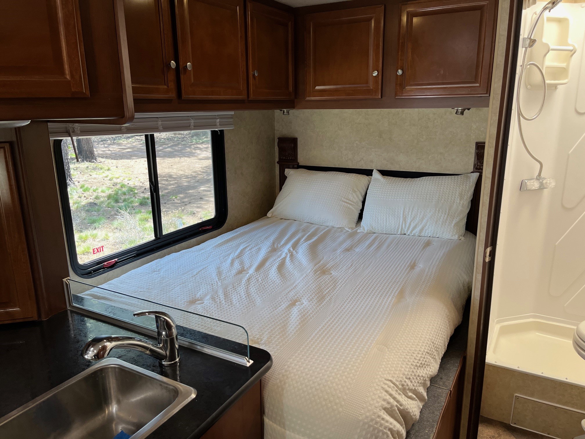 Inside an RV rental: a neat bedroom with white bedding, functional sink area, and part of the shower visible.. Jamboree Searcher 2013