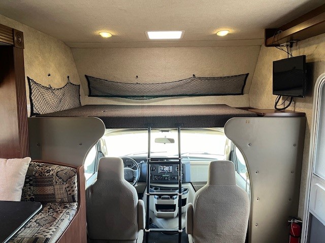 RV rental interior: overhead bunk bed with storage nets, driver's cabin, dinette, and TV. Ready for your adventure.. Jamboree Searcher 2013