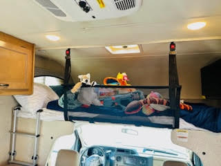 Inside an RV rental, a netted bunk bed holds plush toys above a lower sleeping area, accessible by ladder.. Thor Four Winds 2021