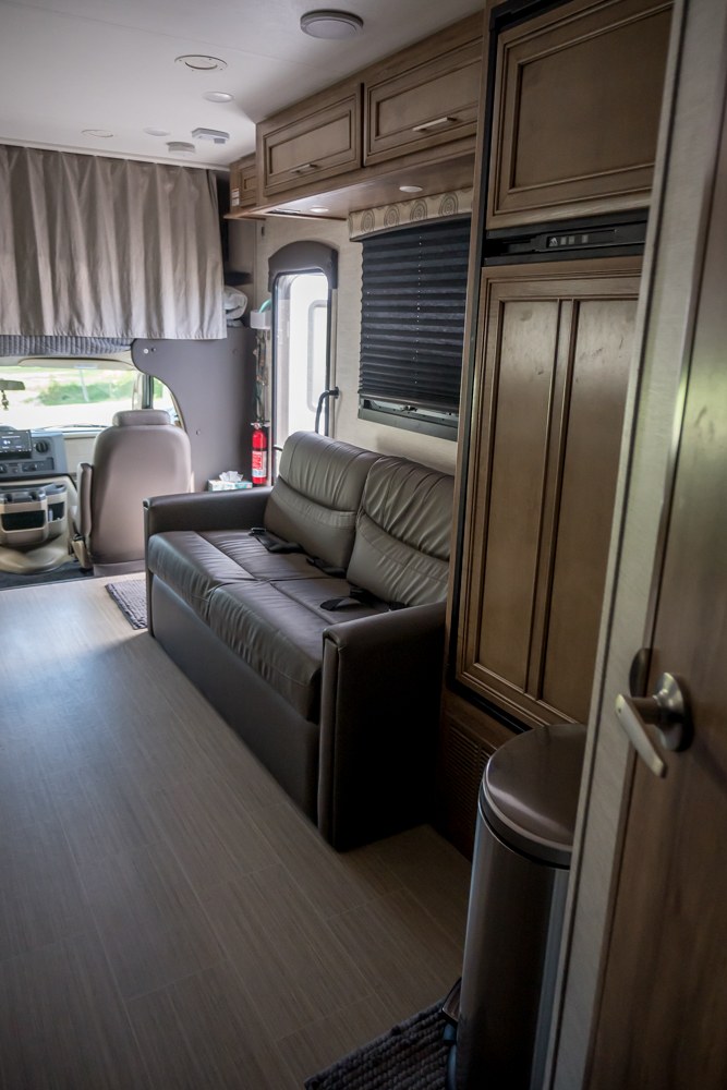 Modern rv rental interior: brown sofa, light wood-style flooring, and built-in cabinets provide a comfortable travel space.. Entegra Coach Odyssey 2021