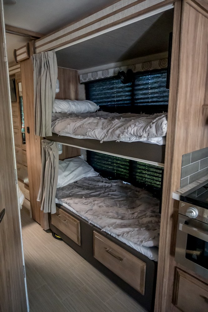 Inside an RV rental: two comfy bunk beds with privacy curtains, window blinds, & under-bed storage drawers.. Entegra Coach Odyssey 2021