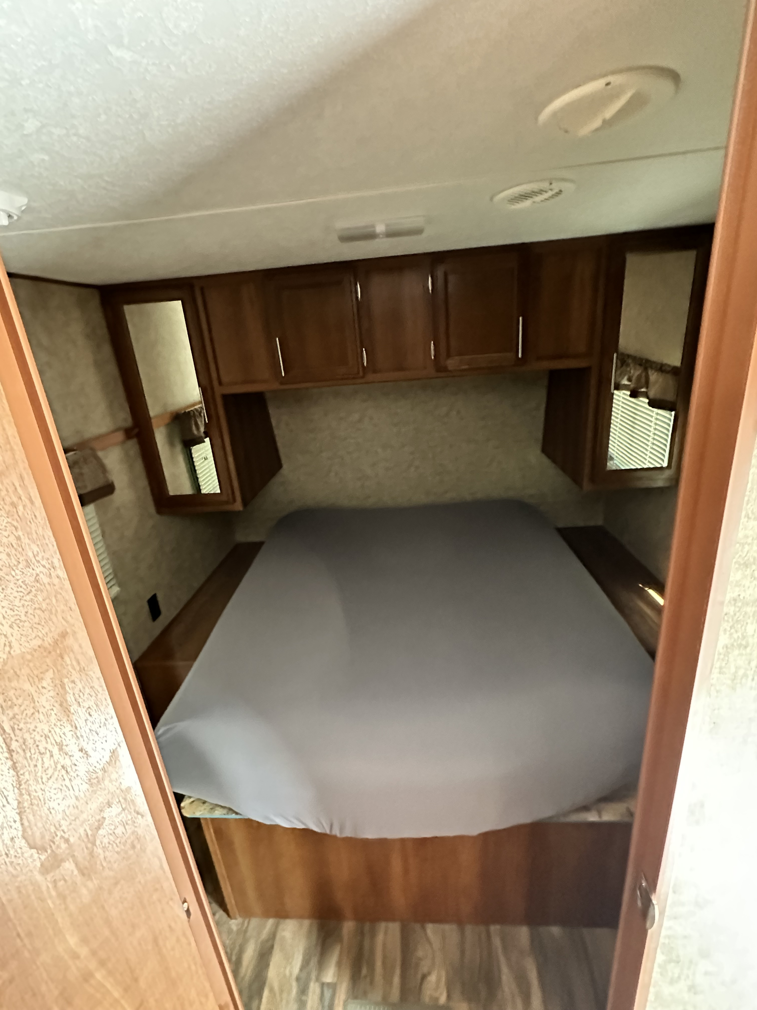 Cozy RV rental bedroom featuring a bed, ample storage via overhead cabinets, and mirrored wardrobes.. Avenger ATI 2018