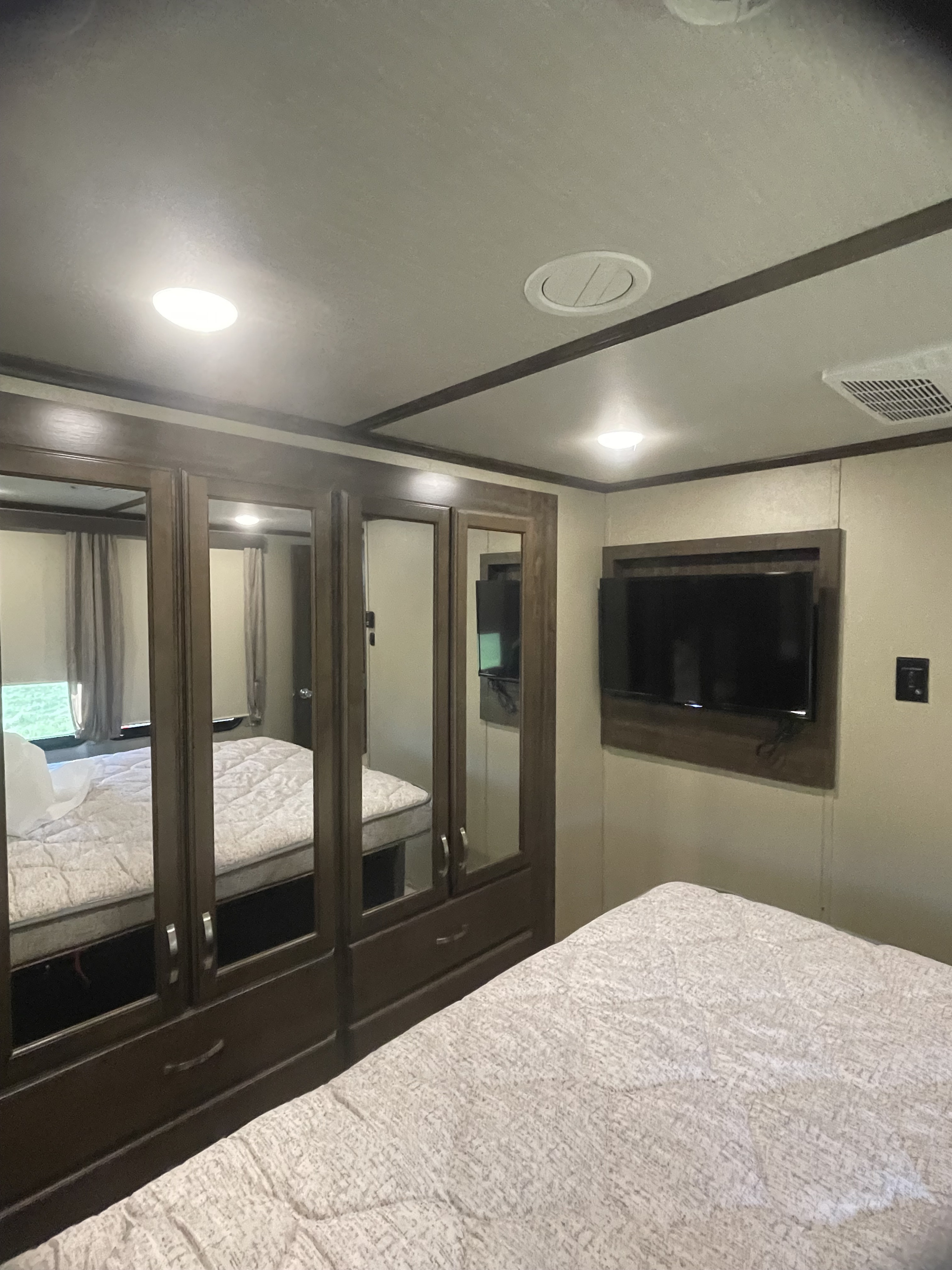 RV rental bedroom interior: features a large mirrored wardrobe, wall-mounted TV, and a cozy bed with a patterned comforter.. Grand Design Solitude Toy Hauler 2018