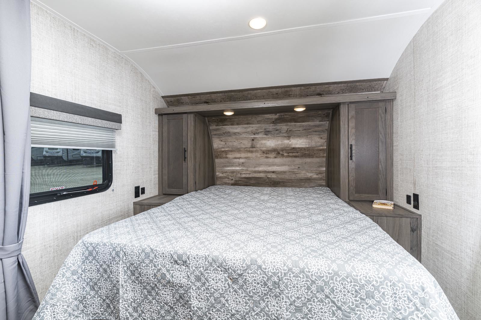 Inside this RV rental, a comfy bedroom features a bed with a patterned quilt, rustic wood headboard, cabinets, and a window.. Gulf Stream Friendship 2022