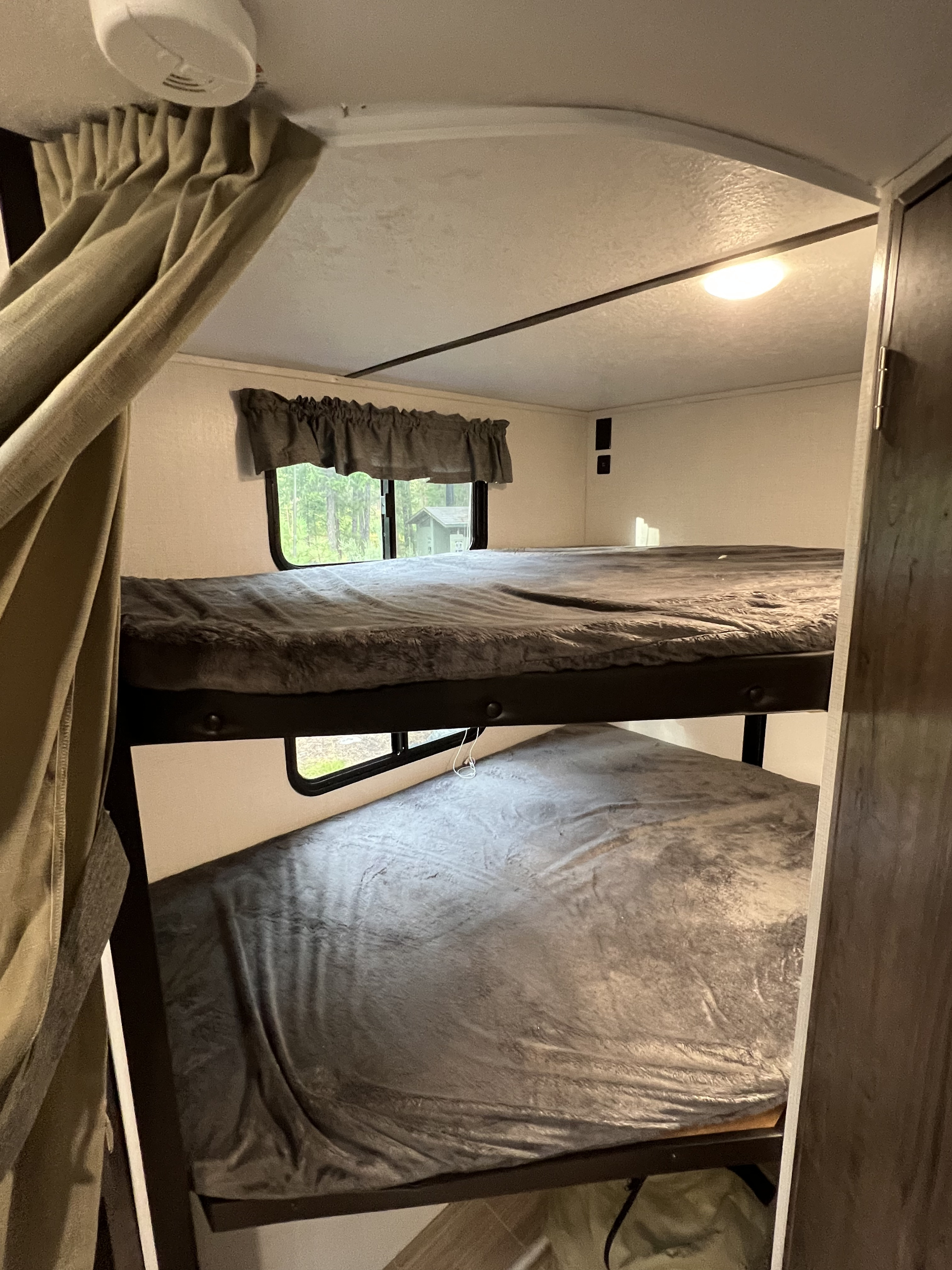 RV rental interior showing two bunk beds with soft grey blankets and a window overlooking nature.. Keystone Passport 2021