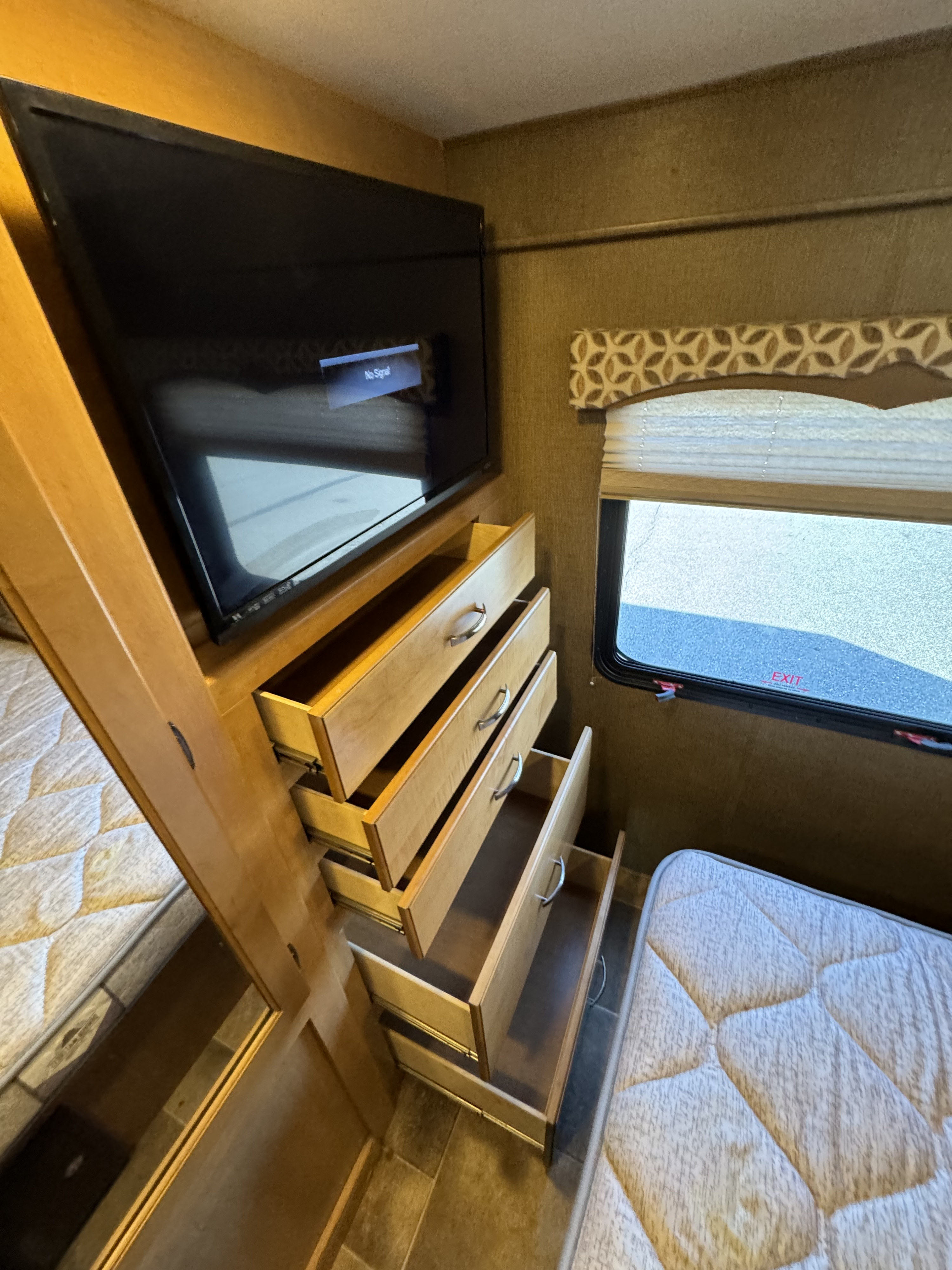 RV rental bedroom with multiple beds, a mounted TV showing no signal, and open wooden drawers for storage.. Jayco Greyhawk 2014