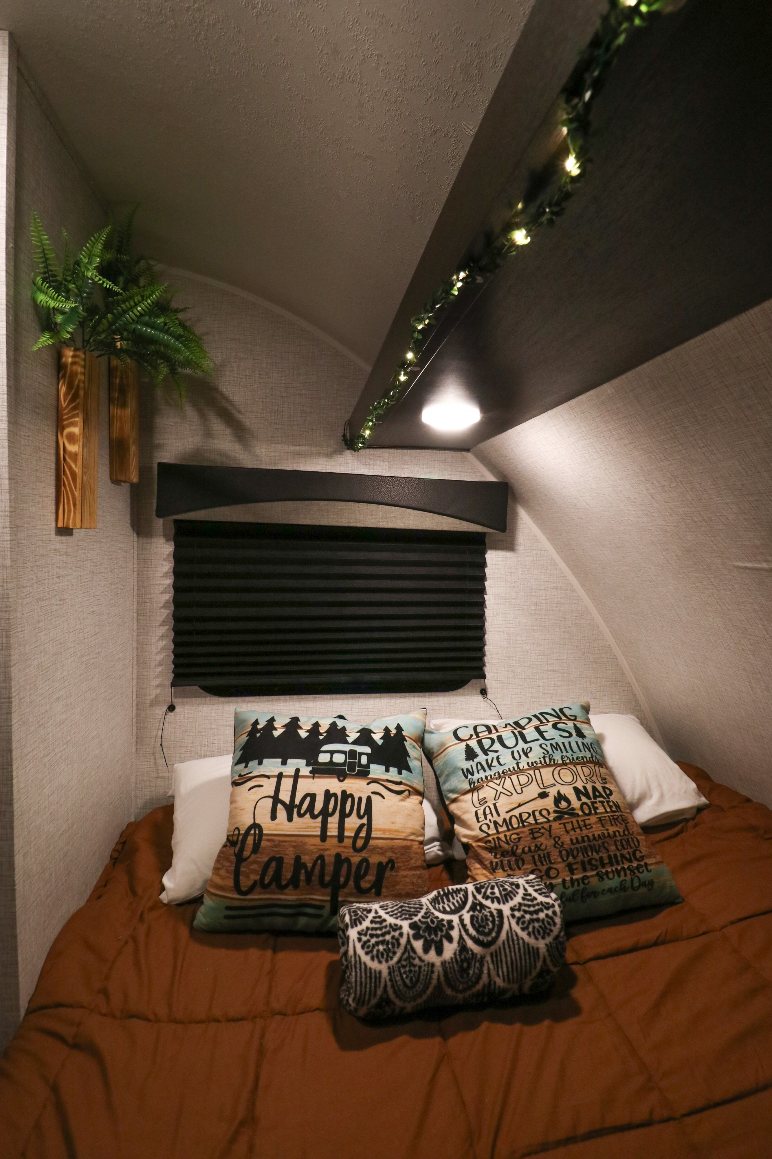 Cozy RV rental bedroom featuring a bed with "Happy Camper" pillows, warm brown bedding, and decorative string lights.. Braxton Creek Bushwacker Plus 17BH 2023
