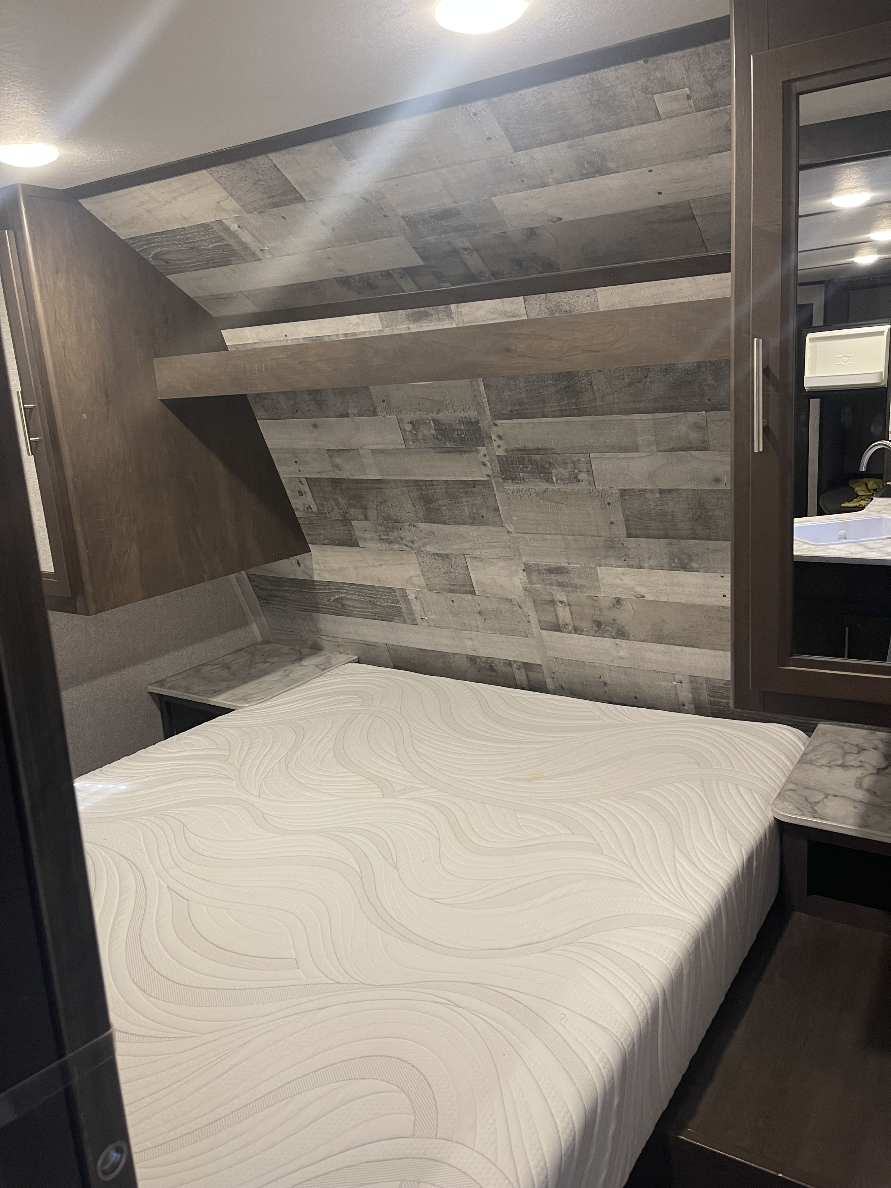 Experience comfort in this RV rental bedroom: a large bed, stylish wood paneling, and a mirrored closet reflecting a sink vanity.. Coleman 262BH 2021