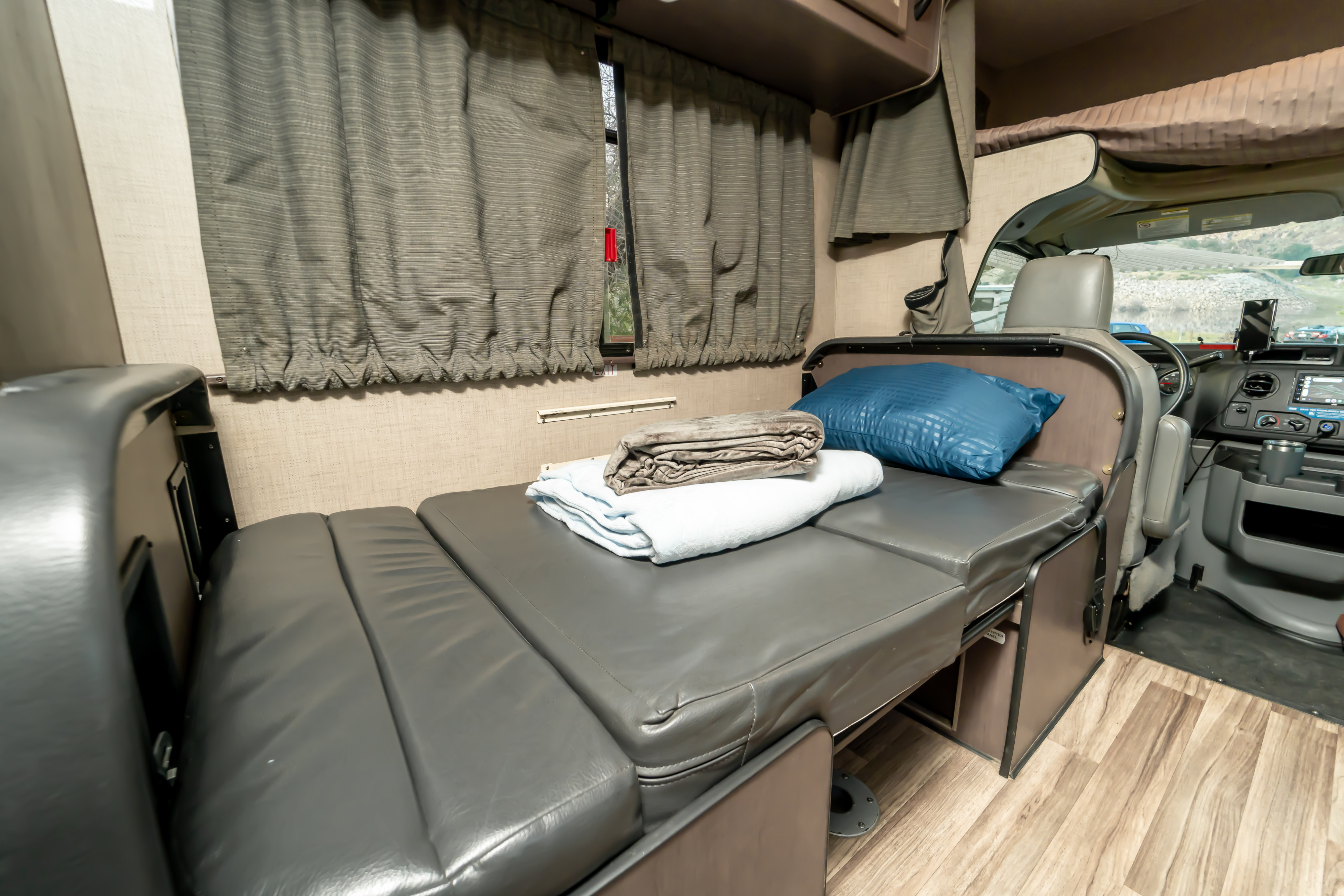 Explore this RV rental's interior. Features a gray convertible bed, bedding, privacy curtains, and the front cockpit.. Thor Majestic 2019