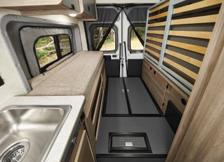 RV rental van interior: A compact living space with a bed on the left, kitchenette, and wood-paneled storage on the right.. Winnebago Solis PX 2025