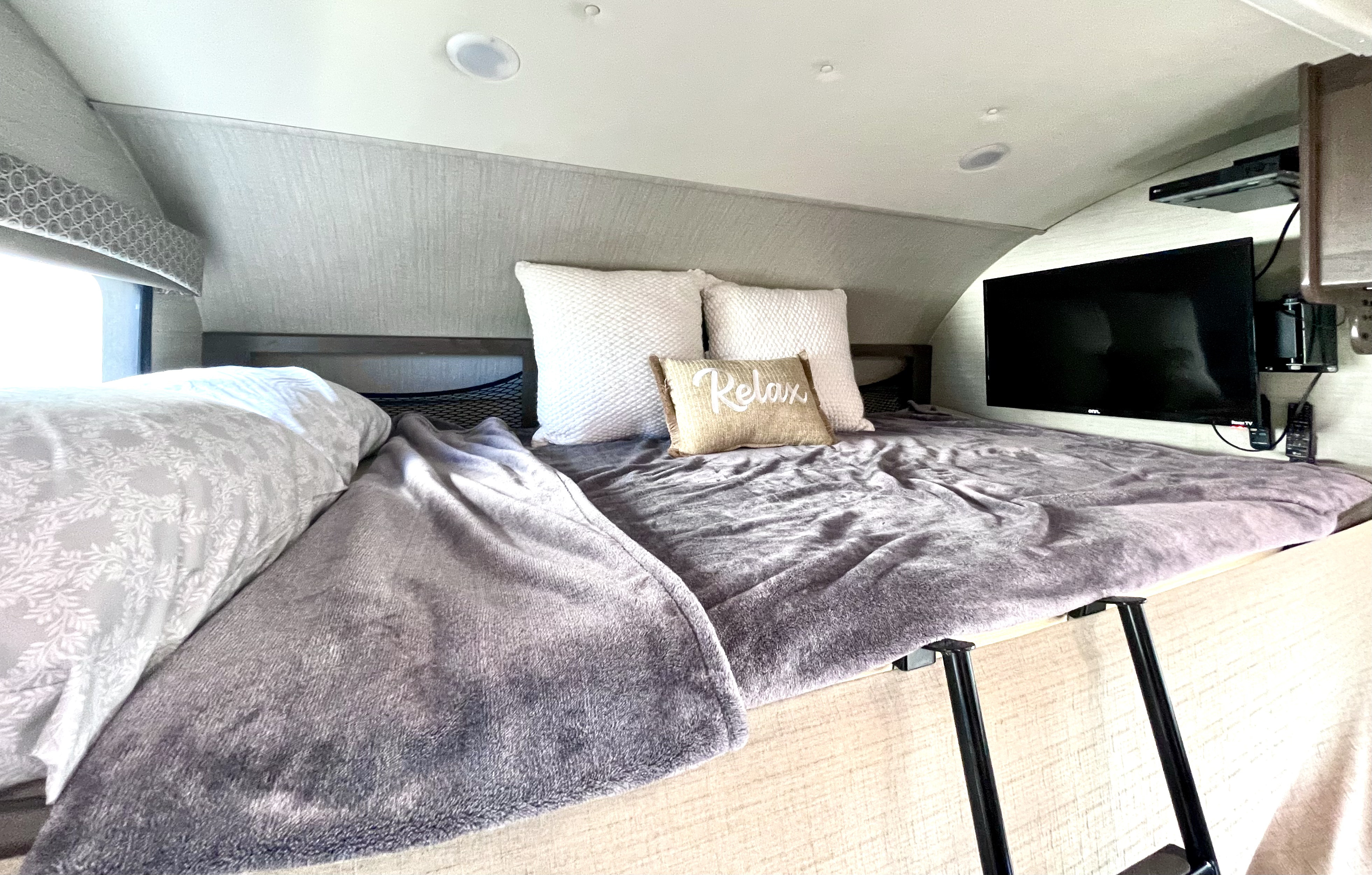 Experience comfort in this RV rental's cab-over bunk. Features a cozy bed, window, TV, and 'Relax' pillow for your journey.. Jayco Greyhawk 2018
