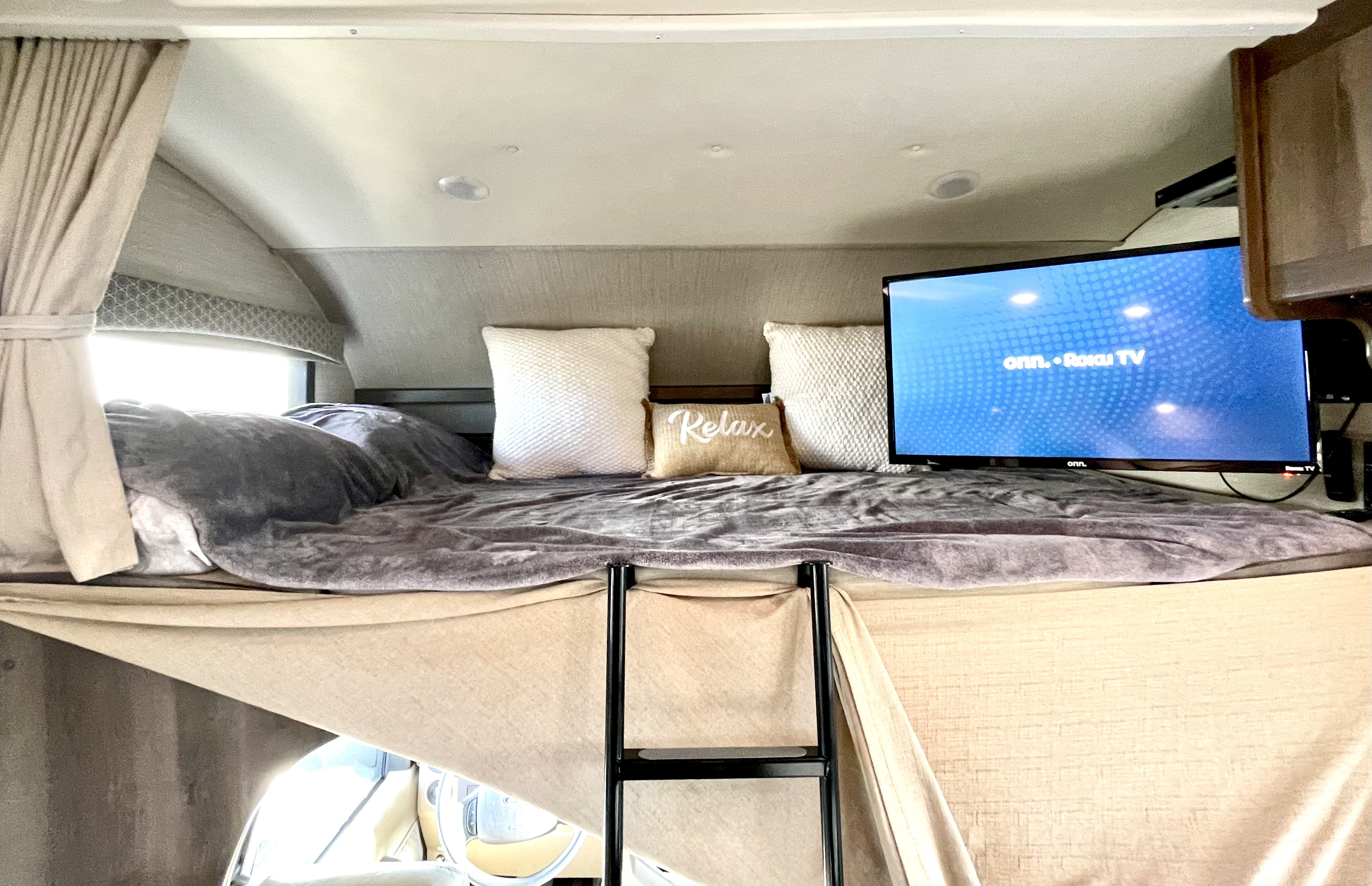 Cozy RV rental cab-over bunk with a TV, blanket, and "Relax" pillow for comfortable stays.. Jayco Greyhawk 2018