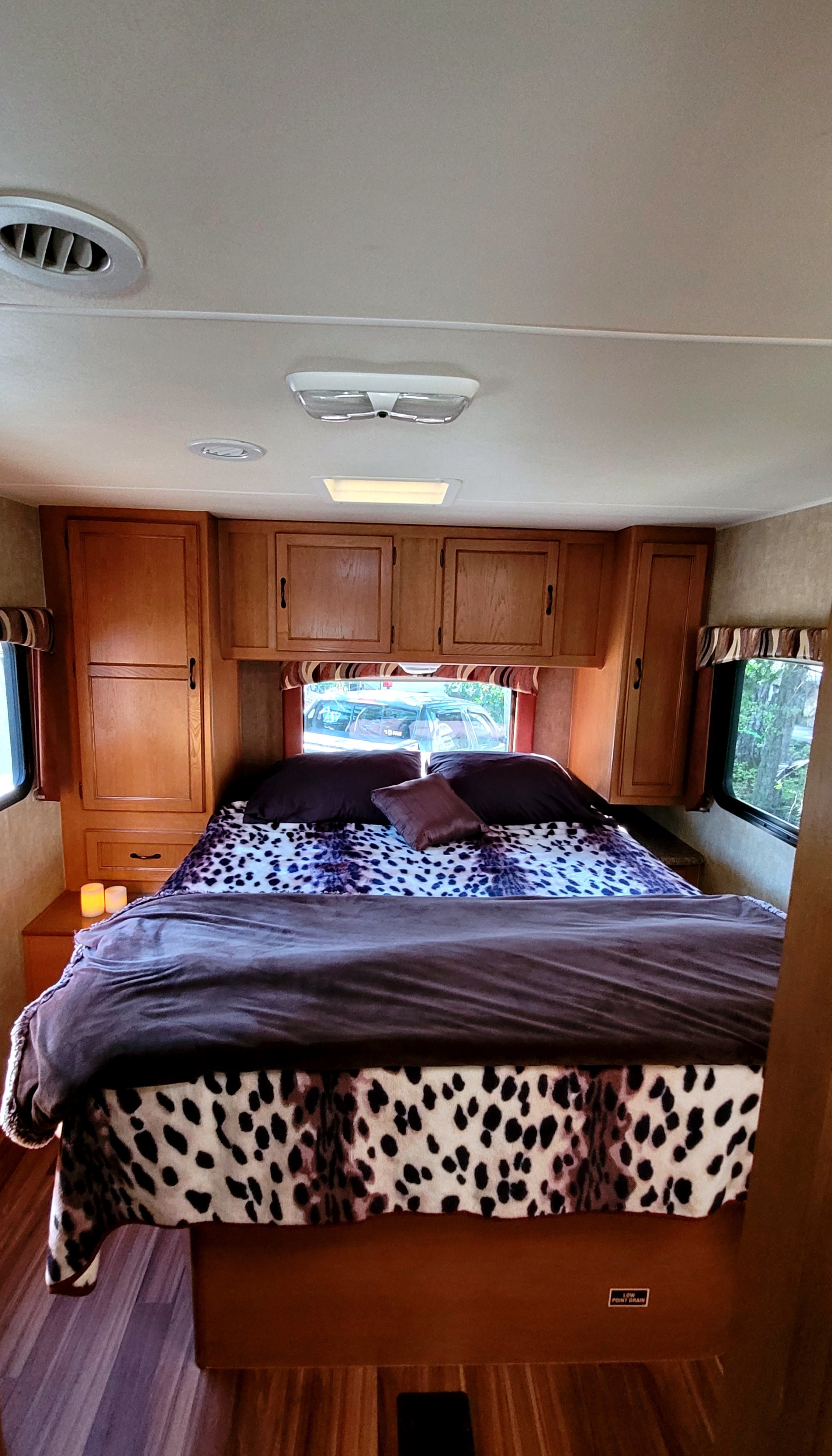 Cozy RV rental bedroom with animal print bedding, built-in wooden cabinets, and large windows. Ideal for compact camper travel.. Forest River Coachmen Freelander 2013