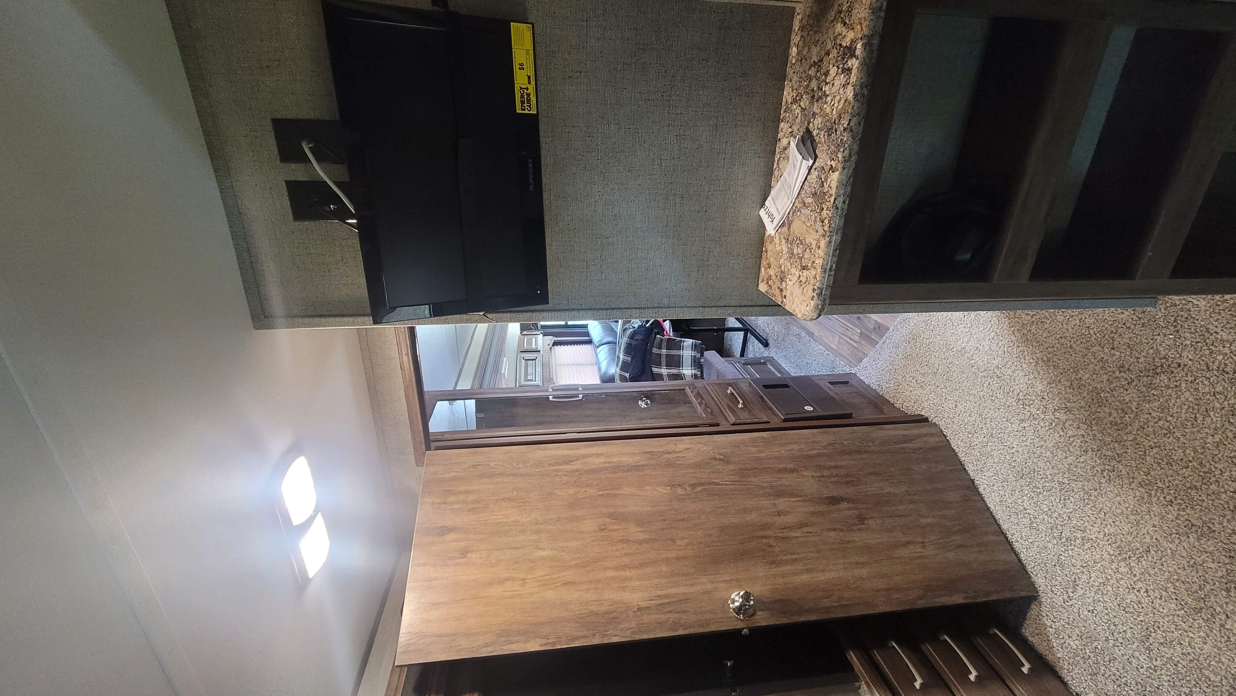 Interior of an RV rental showing a mounted TV, granite-look counter, wood cabinetry, and soft carpet.. Keystone RV Cougar 2017
