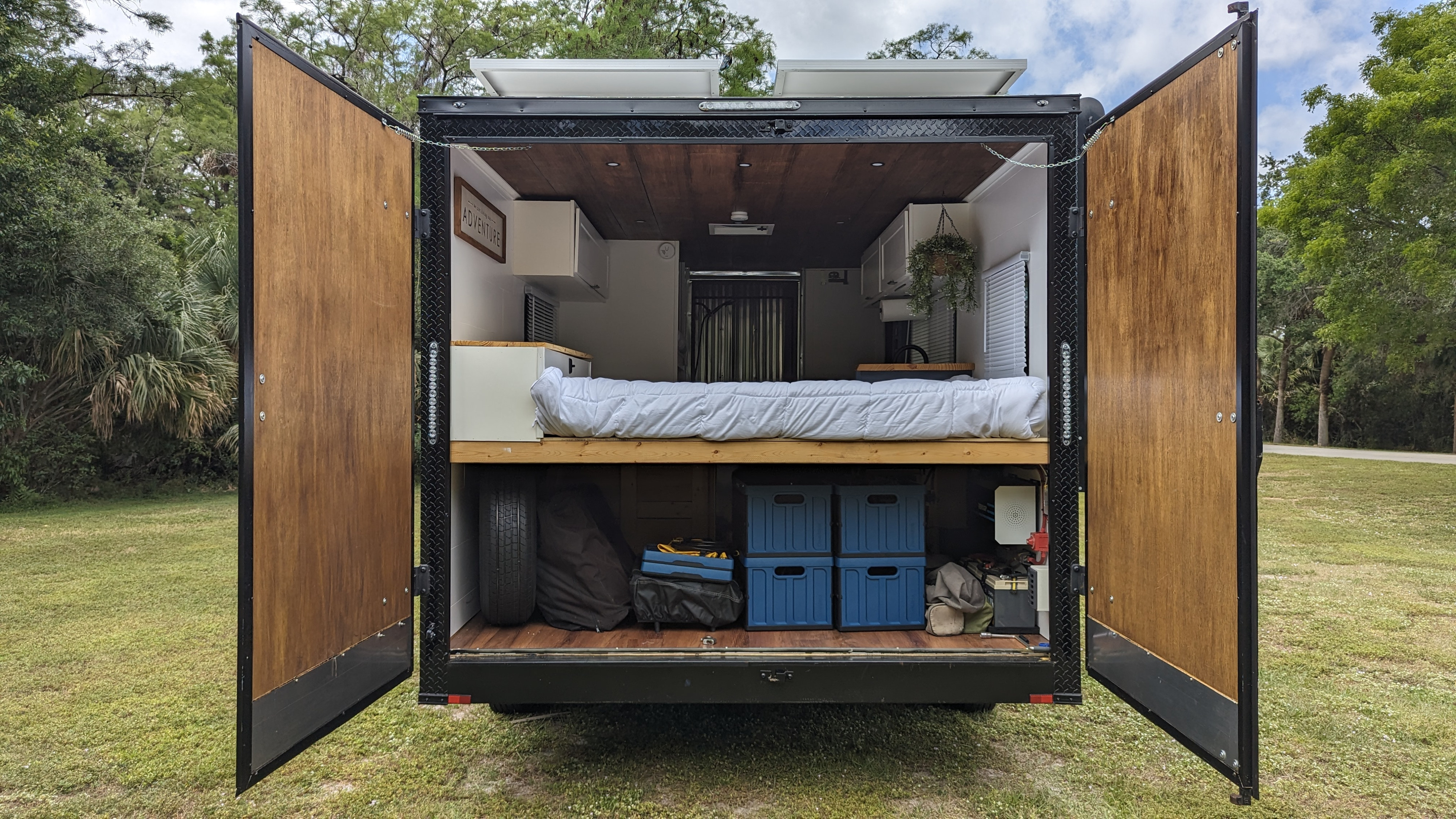 Converted cargo trailer rv rental with rear doors open, revealing a cozy bed, ample storage, and solar panels.. Diamond Cargo 16x8.5 2023