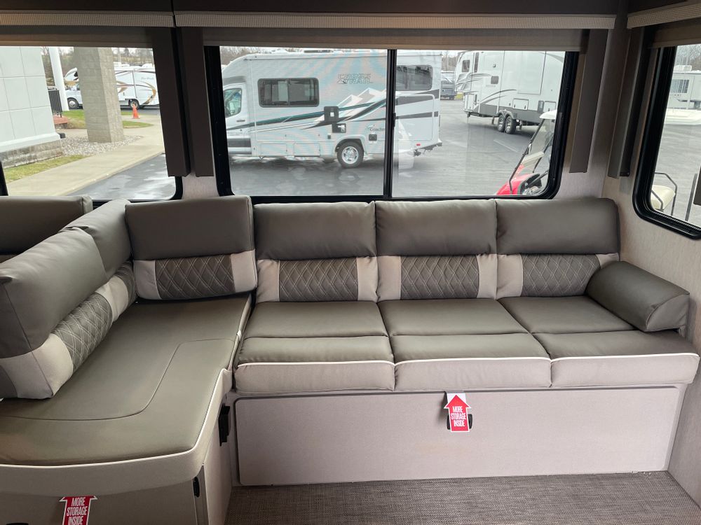 Explore this RV rental's spacious living area with an L-shaped sofa, patterned cushions, and large windows revealing other RVs outside.. Forest River Wildwood 2024
