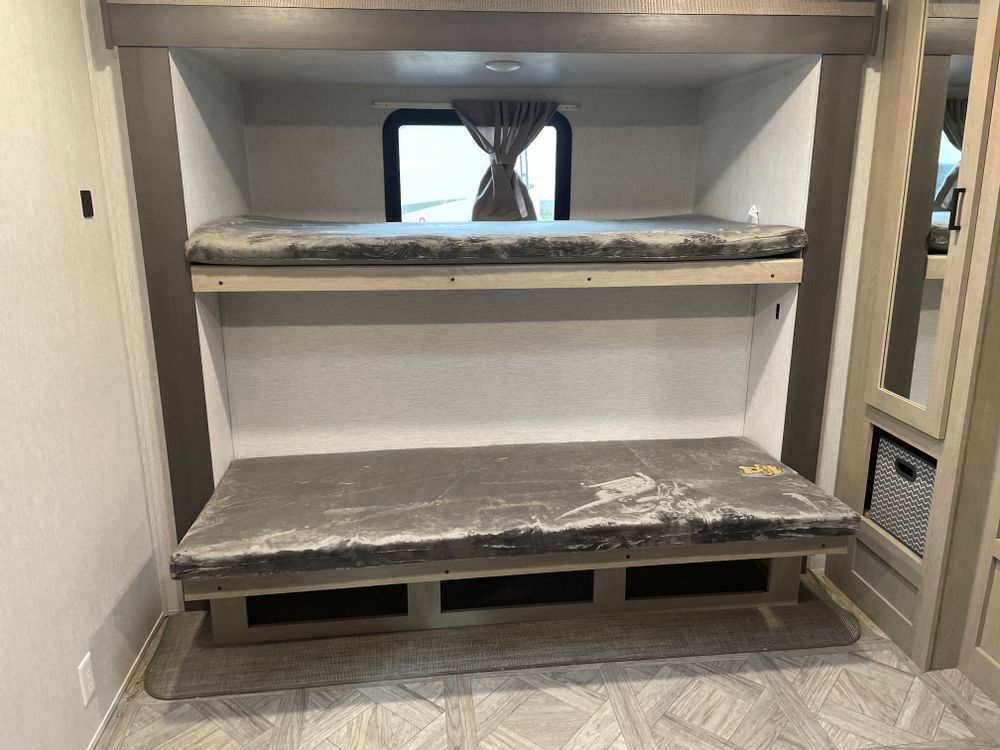 RV rental bunk beds: a neat two-tier sleeping area with mattresses, a window, and shelving for comfort.. Forest River Wildwood 2024