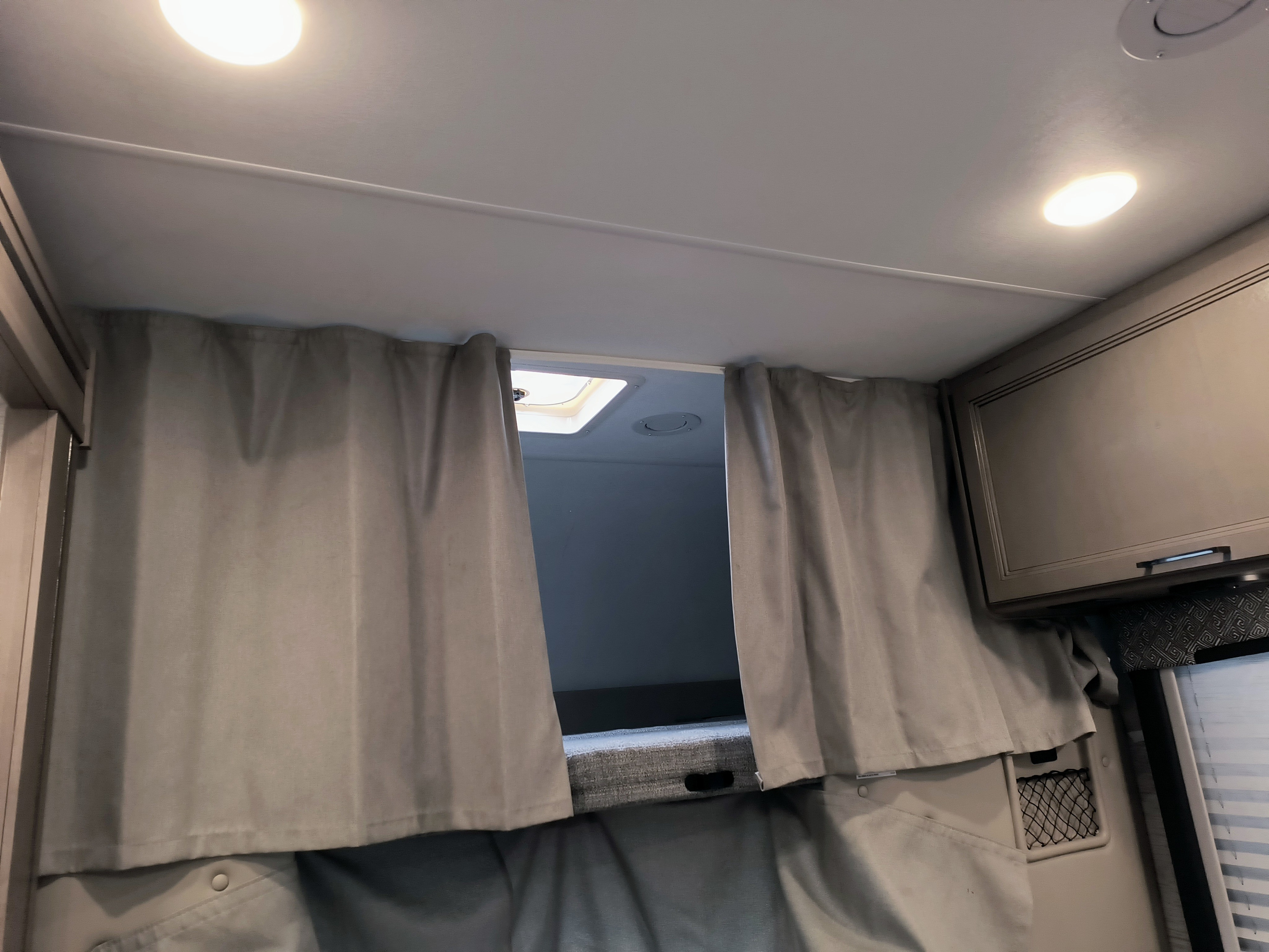 This RV rental shows its bunk bed sleeping area, with gray privacy curtains, bright interior lights, and an overhead vent.. Thor Motor Coach Mgnitude 2022
