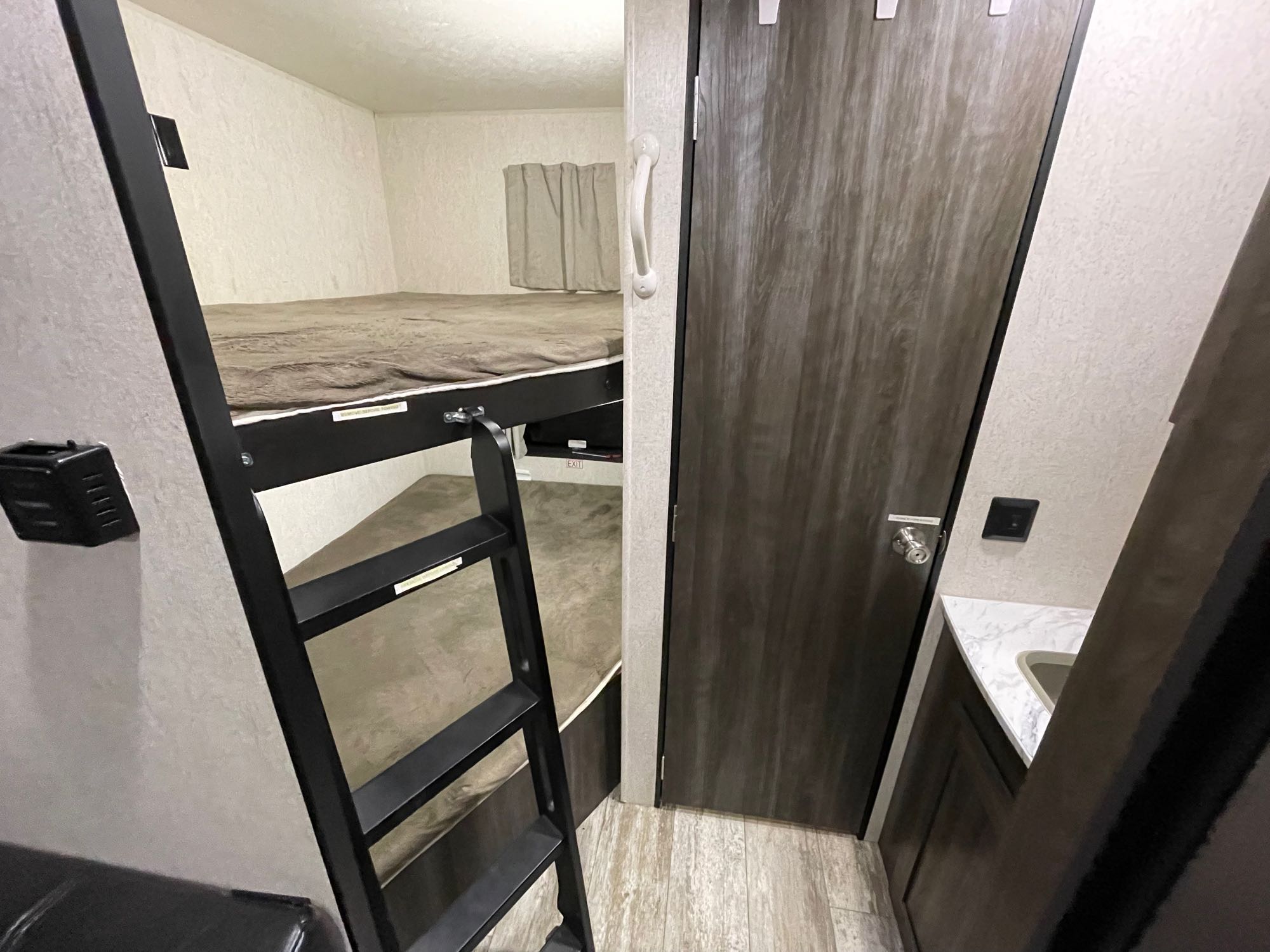 RV rental bunk beds with ladder, beside a wooden door and compact bathroom sink.. Highland Ridge RV Open Range 2019