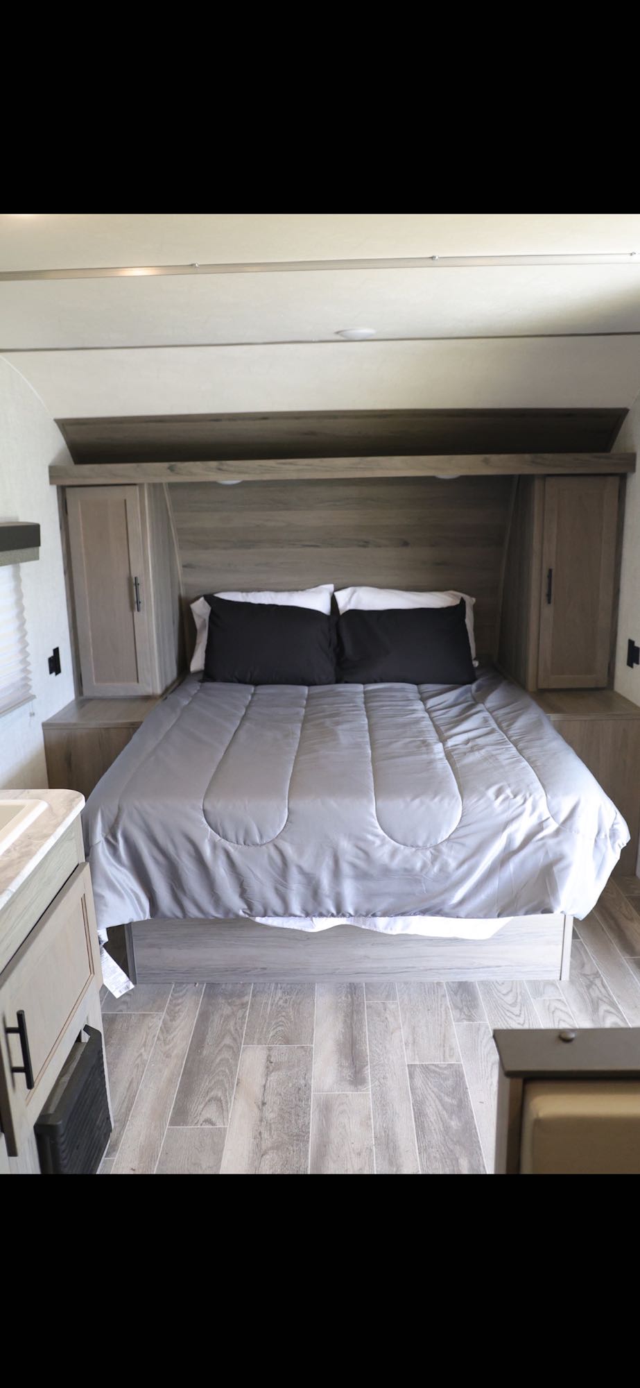 RV rental queen bedroom with modern wood-grain headboard, integrated storage, and light grey bedding.. Gulf Stream Enlighten 2022