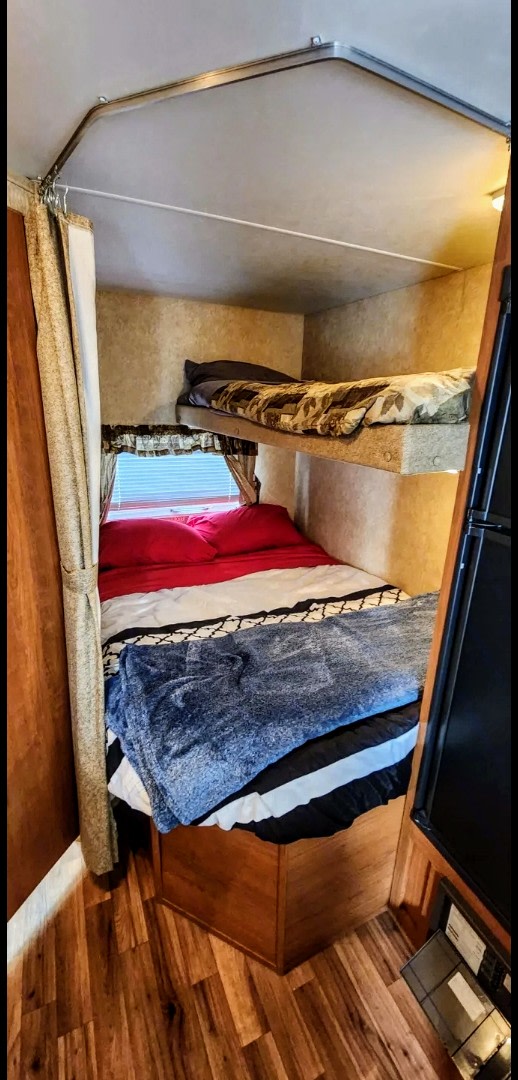 An RV rental interior featuring a compact sleeping space with an upper and lower bunk bed, privacy curtain, and wood laminate floor.. Forest River Wildwood X-Lite 2011