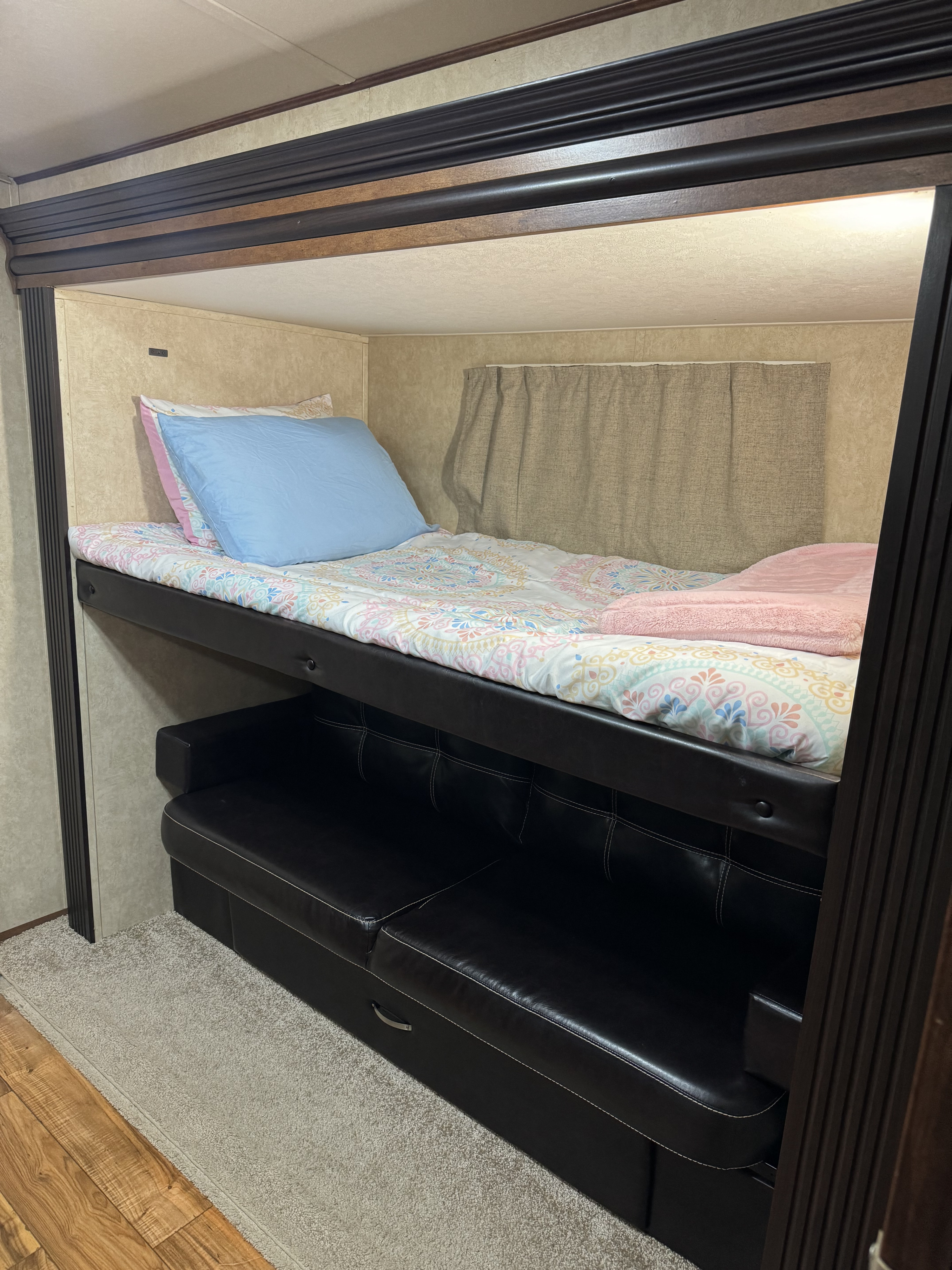 This RV rental features a cozy bunk bed with colorful bedding and a black leather sofa, optimizing compact space.. Forest River Vibe Extreme Lite 2015