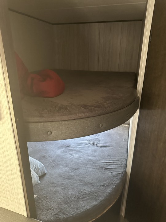 RV rental interior with two cozy bunk beds. Gray bedding, red cushion on top bunk, striped pillows on bottom.. Heartland RVs Pioneer 2020