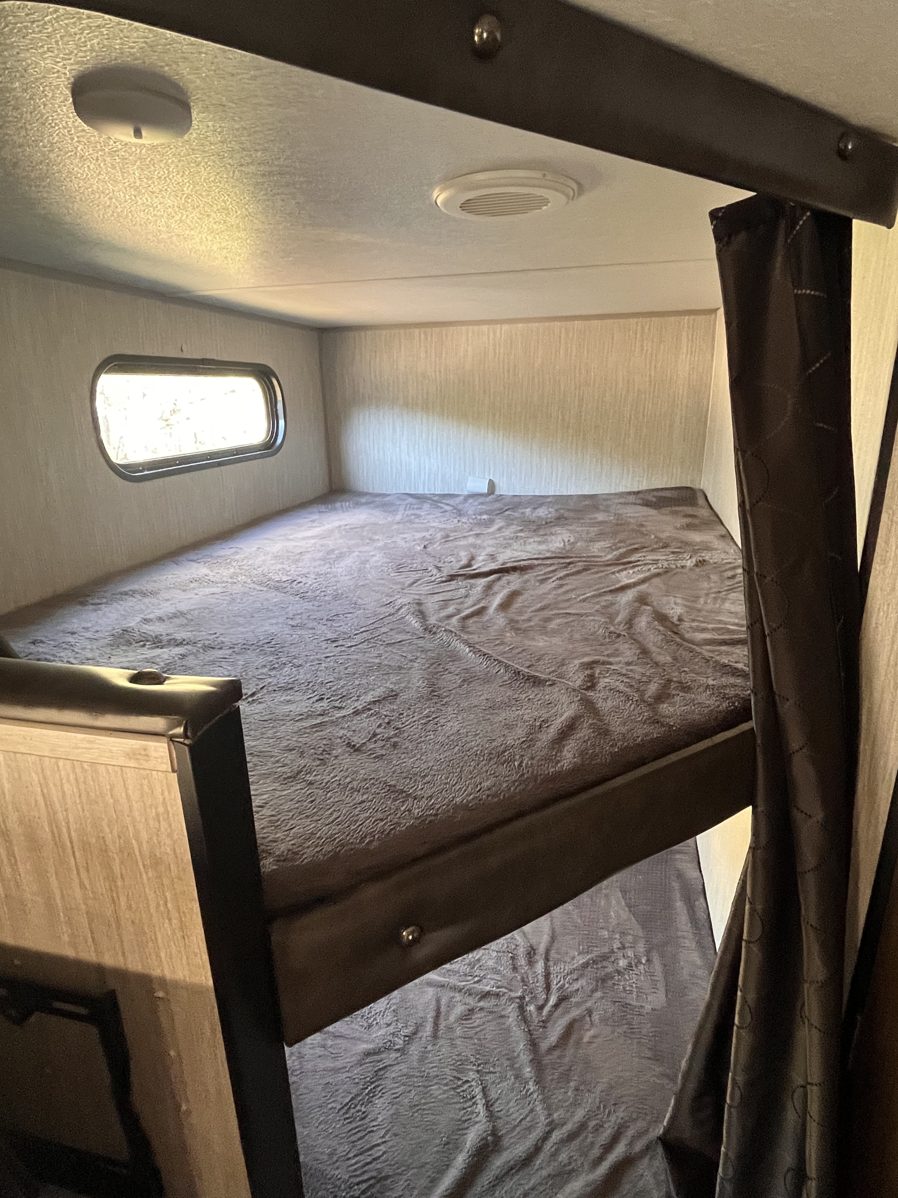 An RV rental's sleeping quarters: Upper bunk bed with window, ceiling light & vent, and dark curtains.. Forest River Cherokee Grey Wolf Special Edition 2020