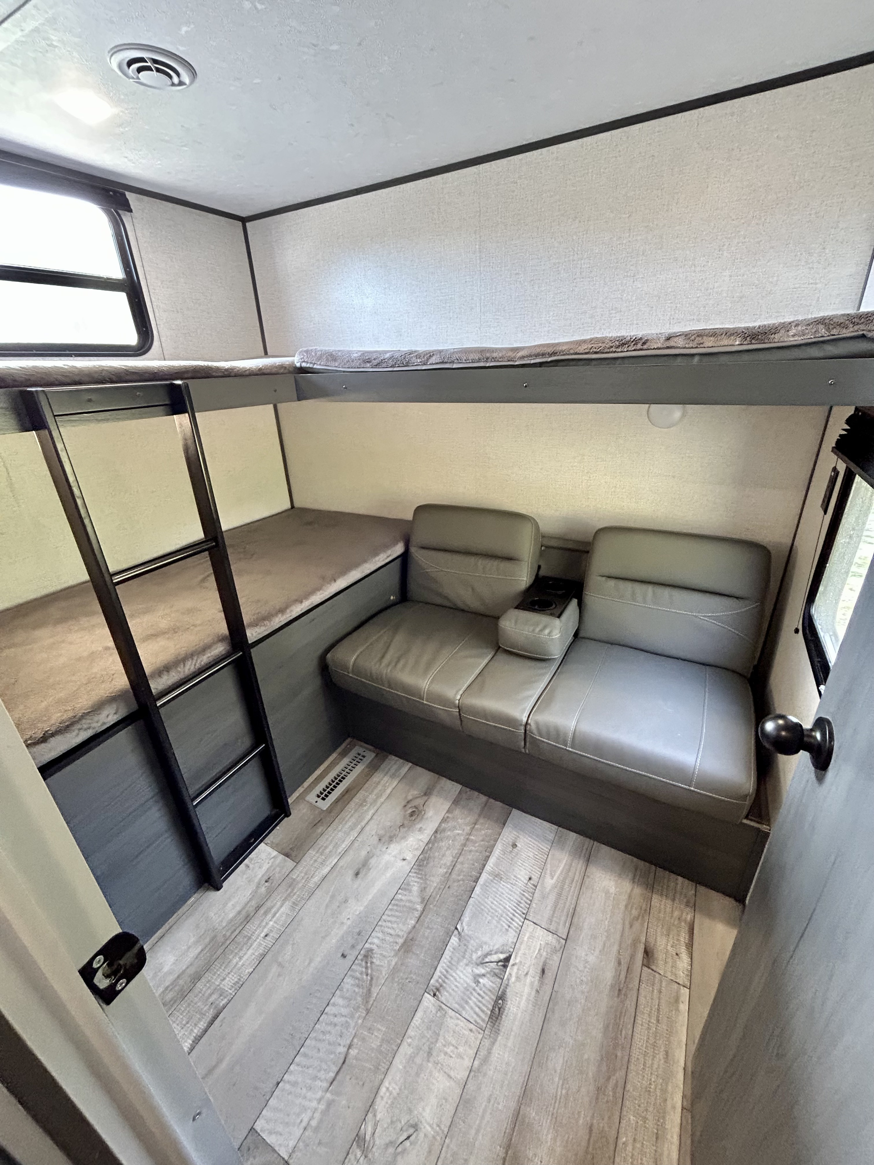 Comfortable bunk beds and sofa seating inside an RV rental. Features ladder, window, and wood-look floor.. Aspen Trail 3280BHS 2022