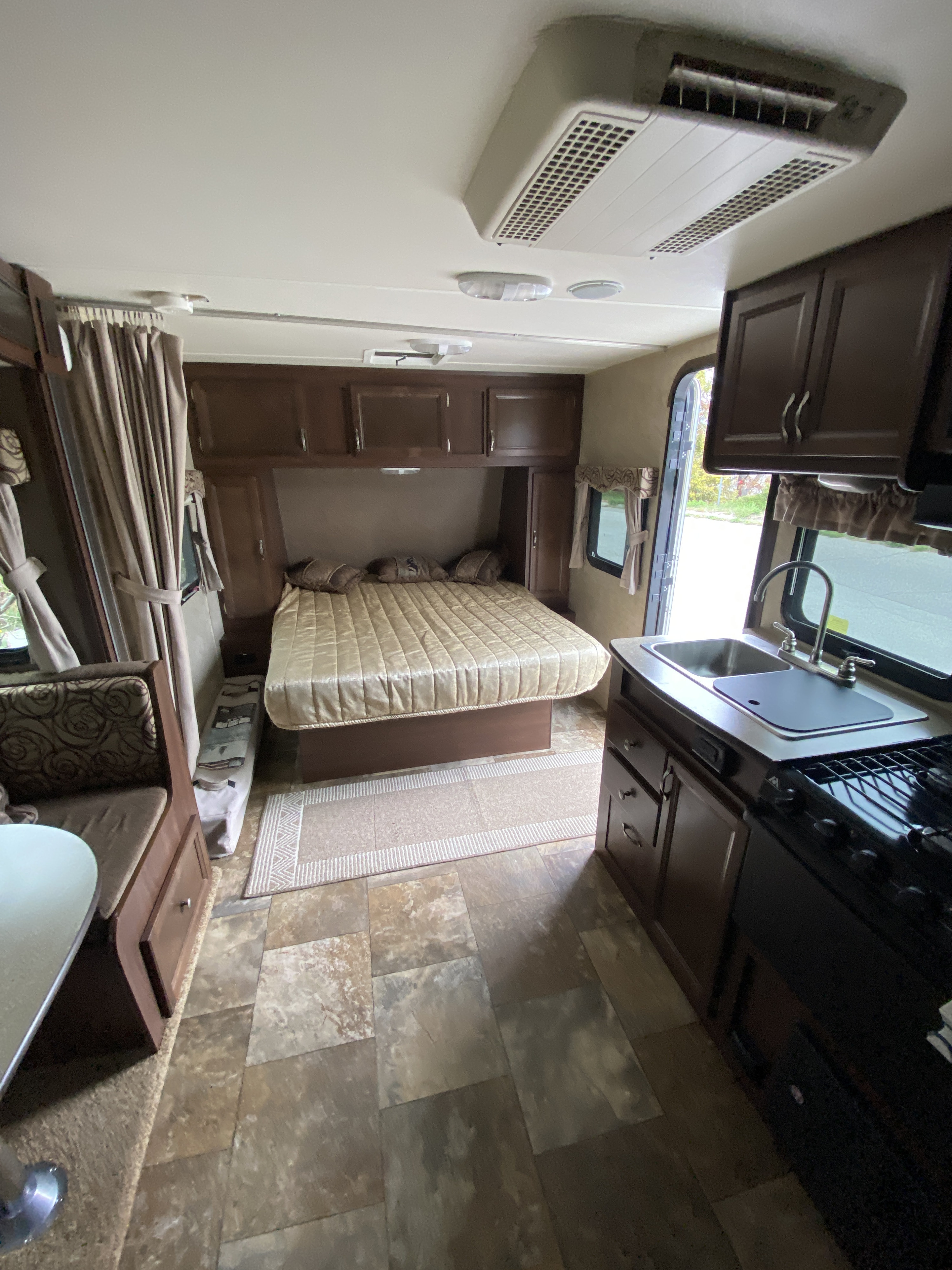 Inside a clean RV rental. Features include a full bed, dinette, and kitchen with sink and stove.. Holiday Rambler 207S 2014