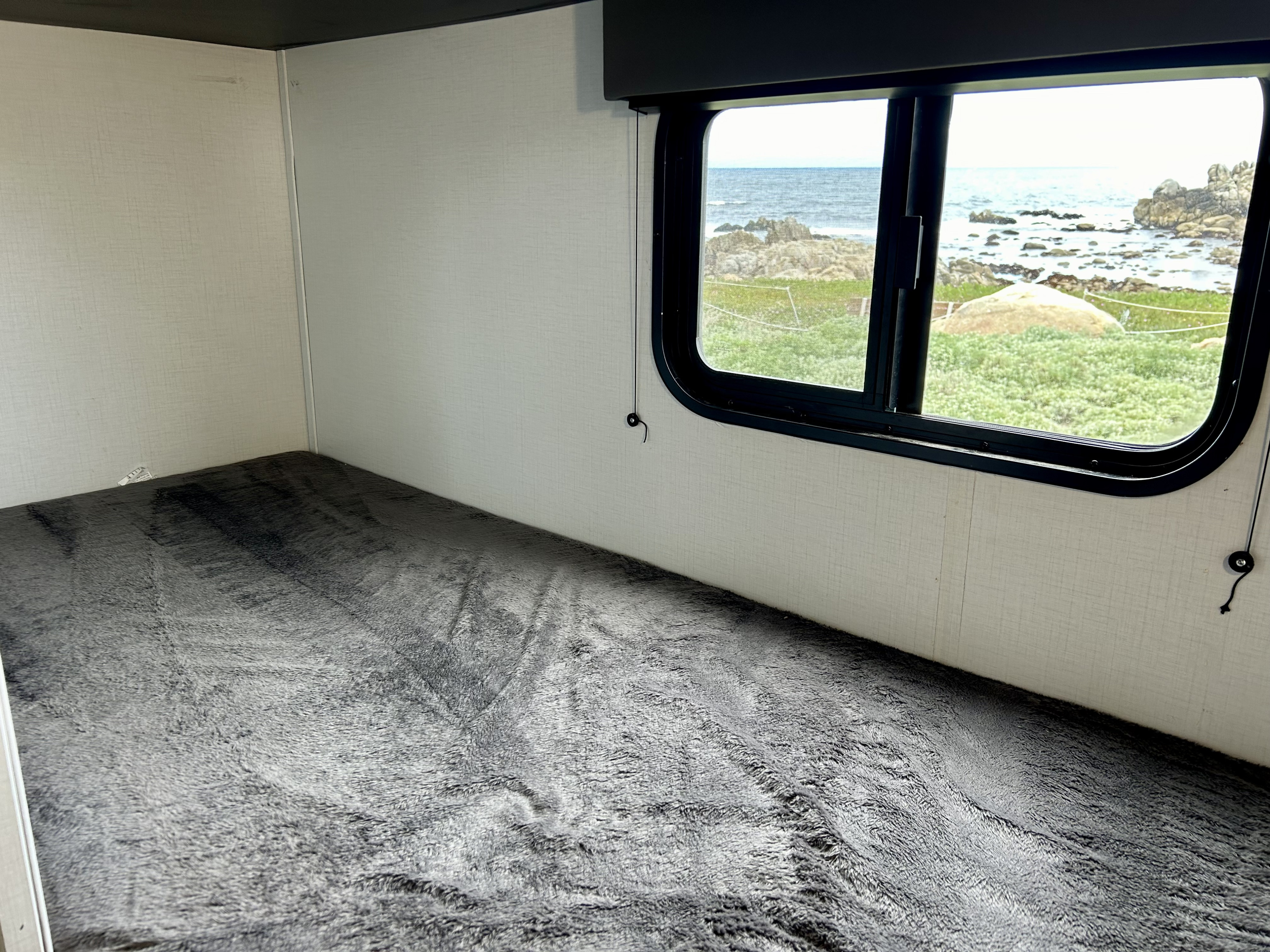 Inside an RV rental: a cozy gray bunk bed offering a beautiful coastal ocean view through the window.. Keystone Springdale 2022