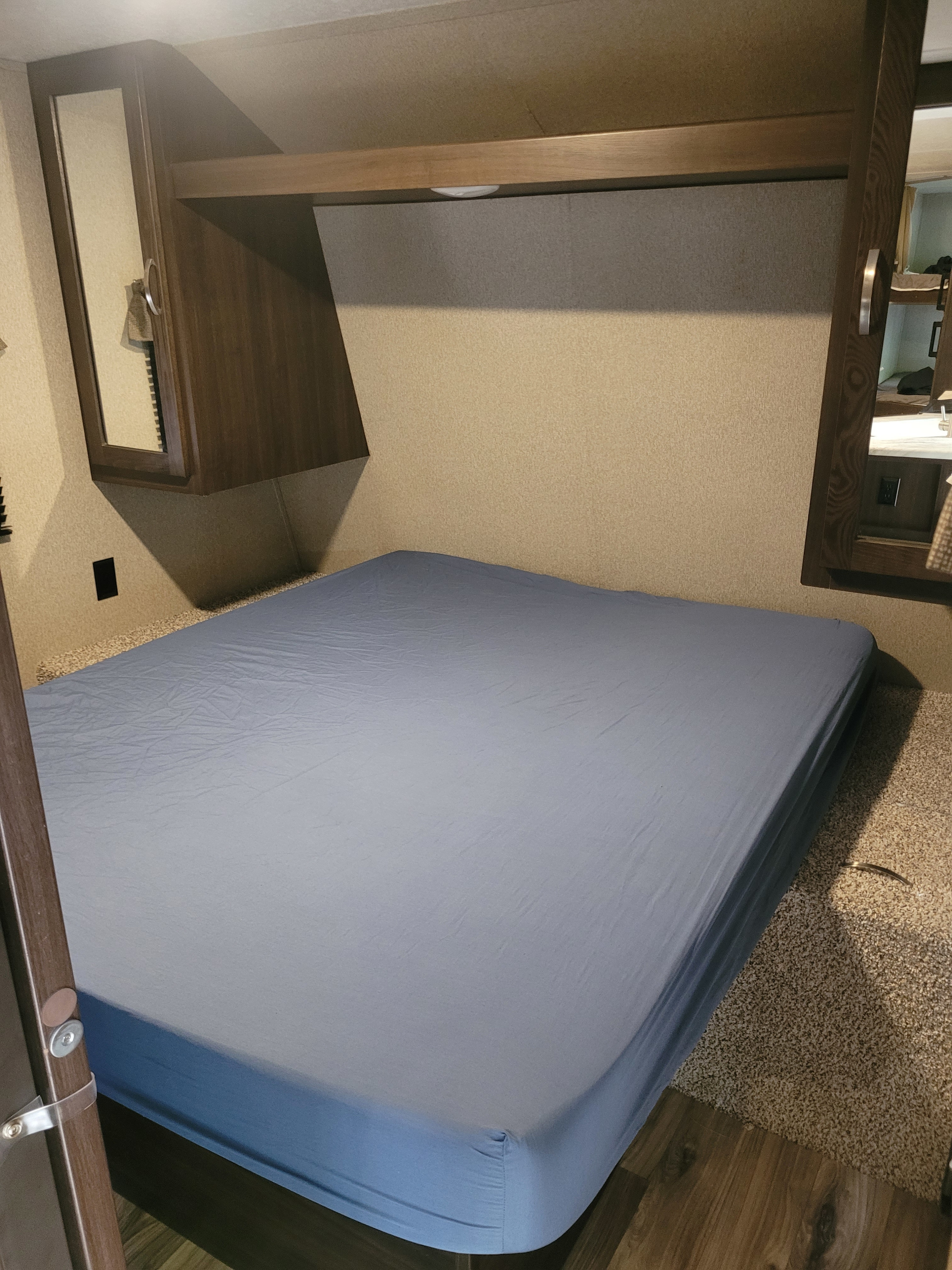 Clean RV rental bedroom with a compact bed, light blue sheet, overhead storage, and wood-paneled cabinets.. Keystone RV Springdale 2020