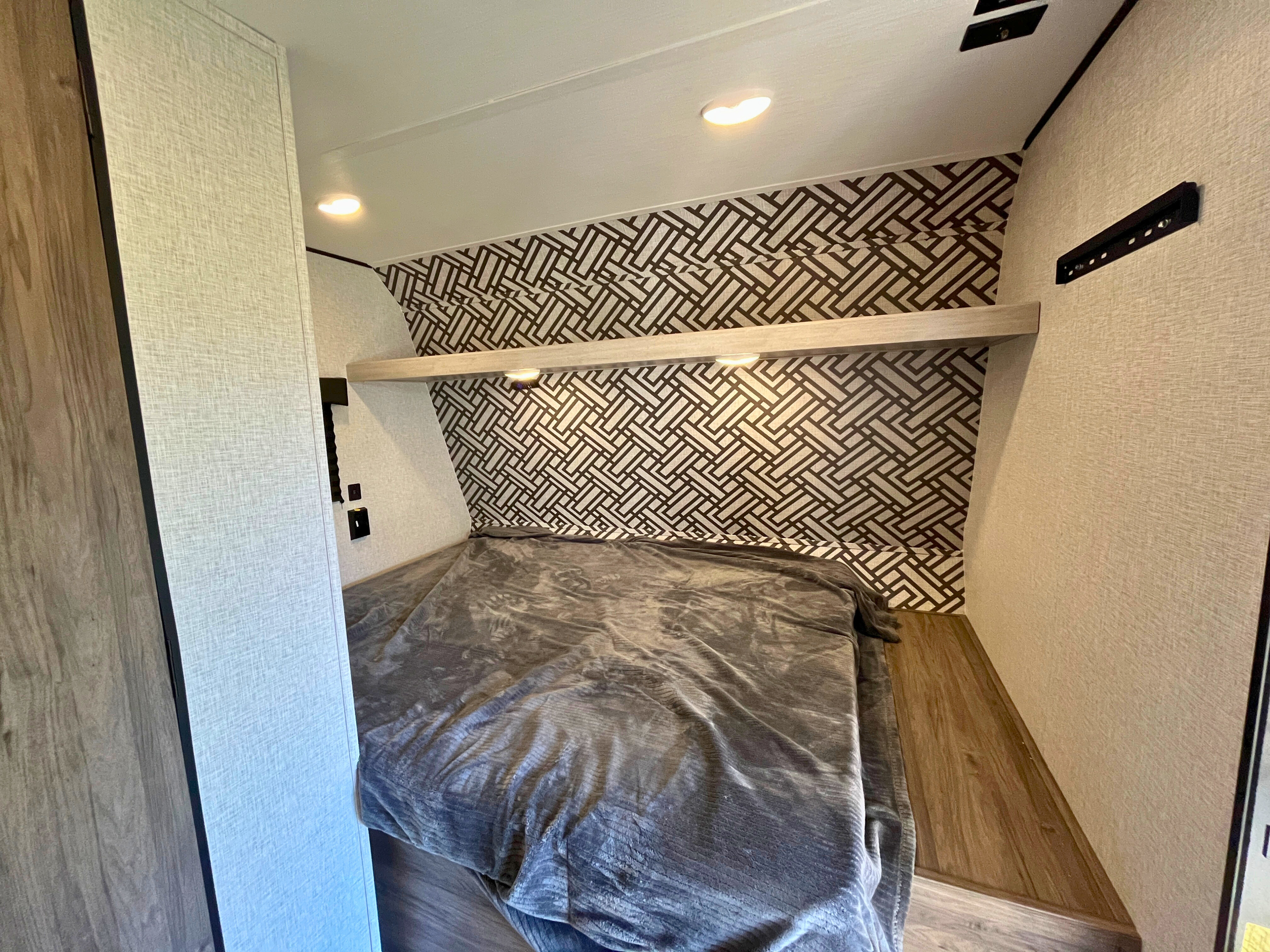 RV rental bedroom: compact space with patterned wall, comfortable bed, and convenient shelf lighting.. Crossroads RV Zinger Lite 2024