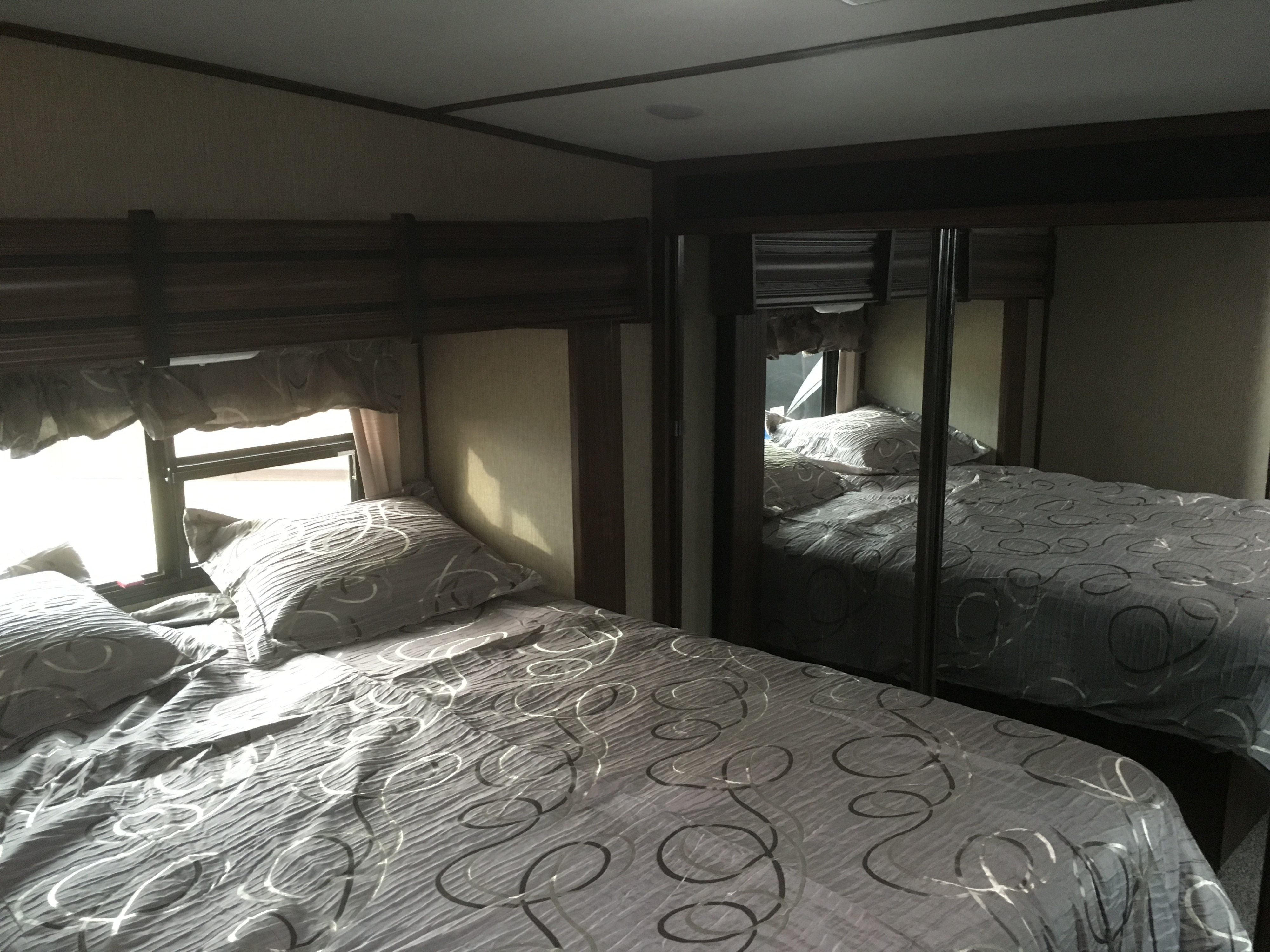 RV rental bedroom: cozy bed with gray bedding, bright window, and mirrored wardrobe.. Keystone Sprinter 2016