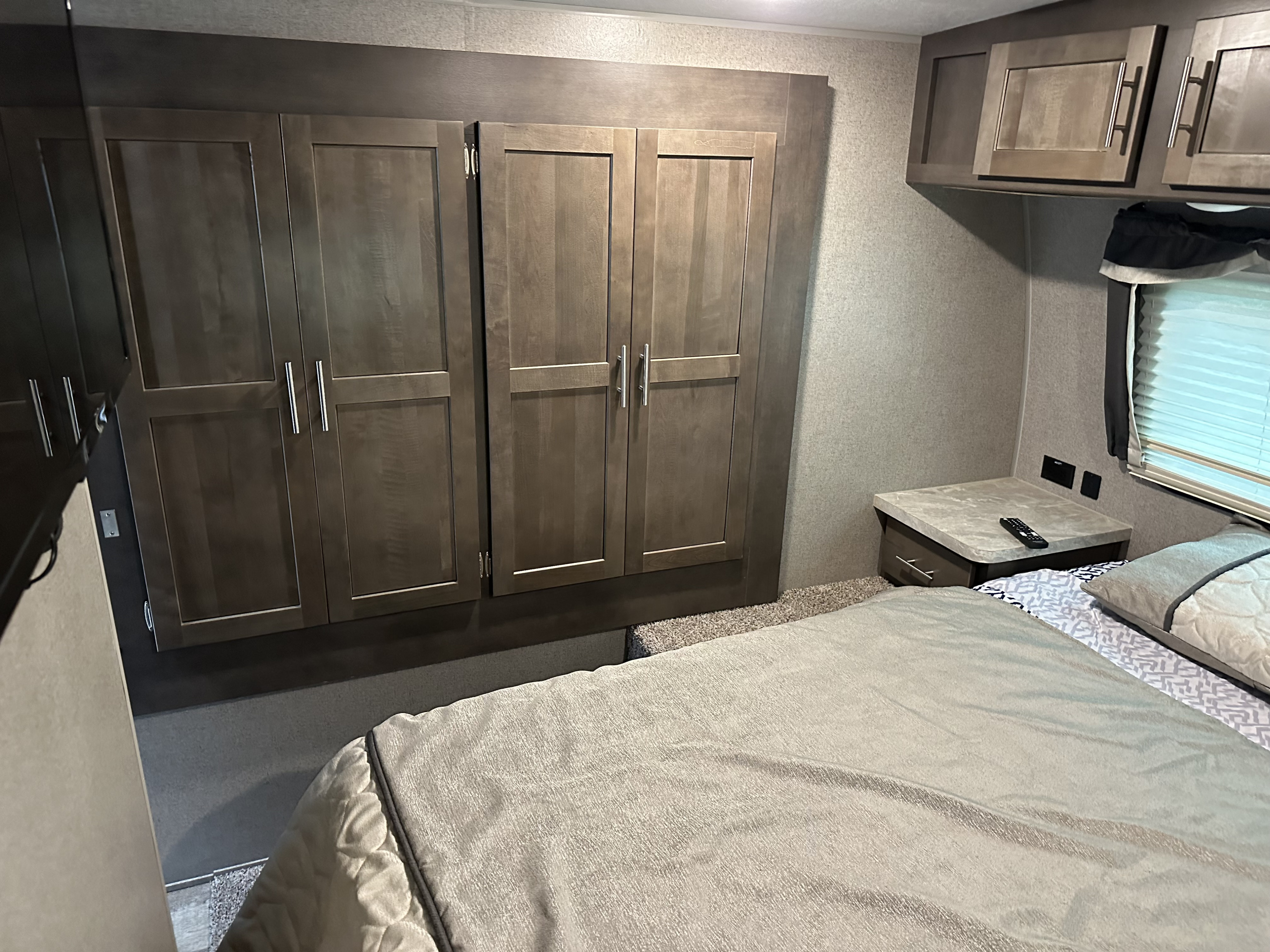 Spacious RV rental bedroom featuring a bed, ample wardrobe, nightstand, and overhead cabinets for comfortable travel.. Forest River Rockwood Ultra Lite 2022