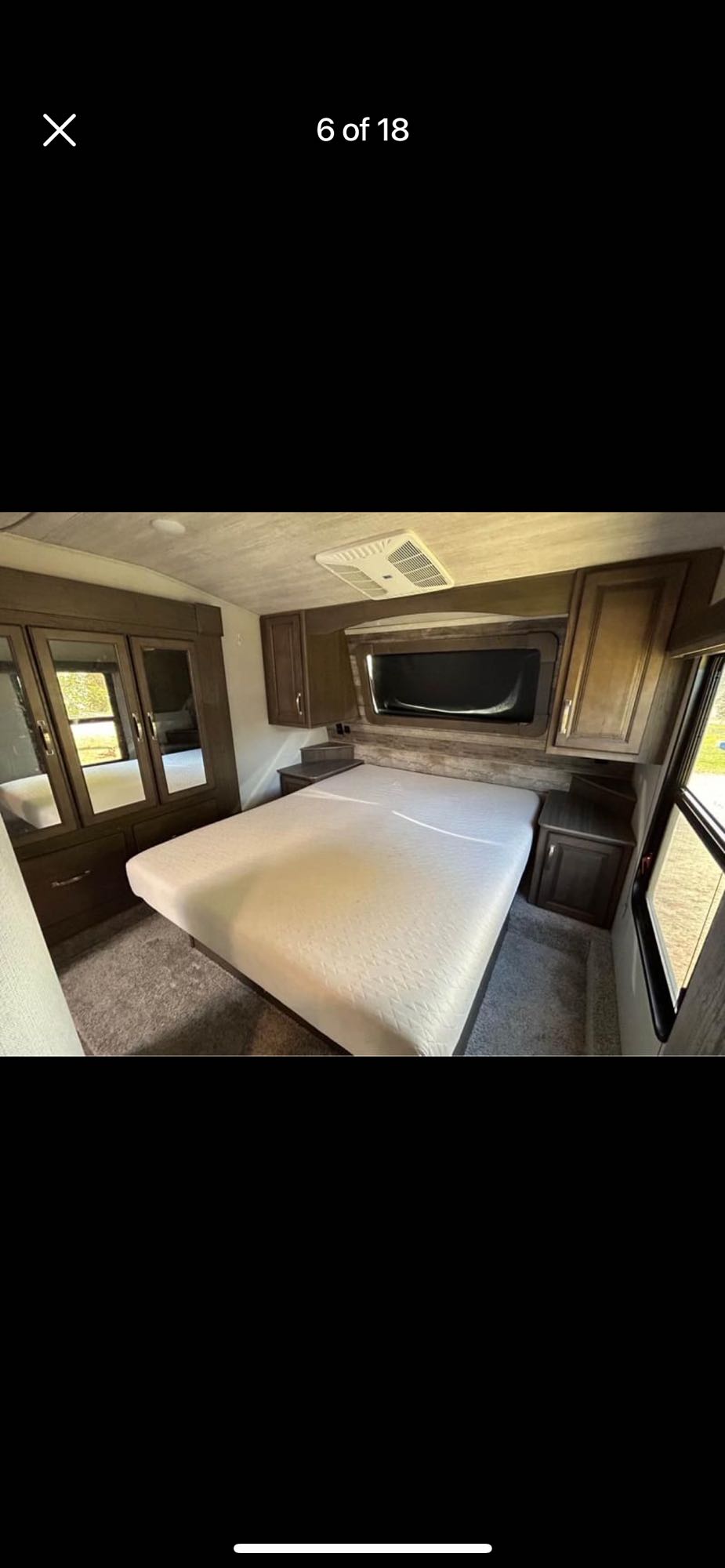 Spacious RV rental bedroom featuring a queen bed, mirrored wardrobe, overhead cabinets, and AC unit for comfortable travel.. Keystone RV Cougar 2021