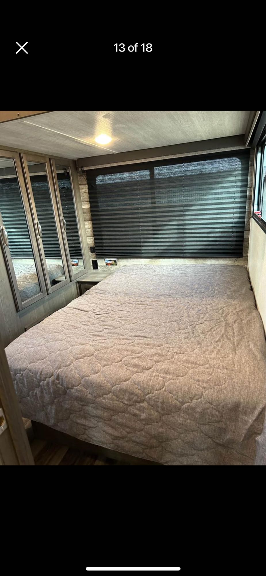 This RV rental offers a compact bedroom with a quilted bed, mirrored cabinets, and wide window blinds.. Keystone RV Cougar 2021