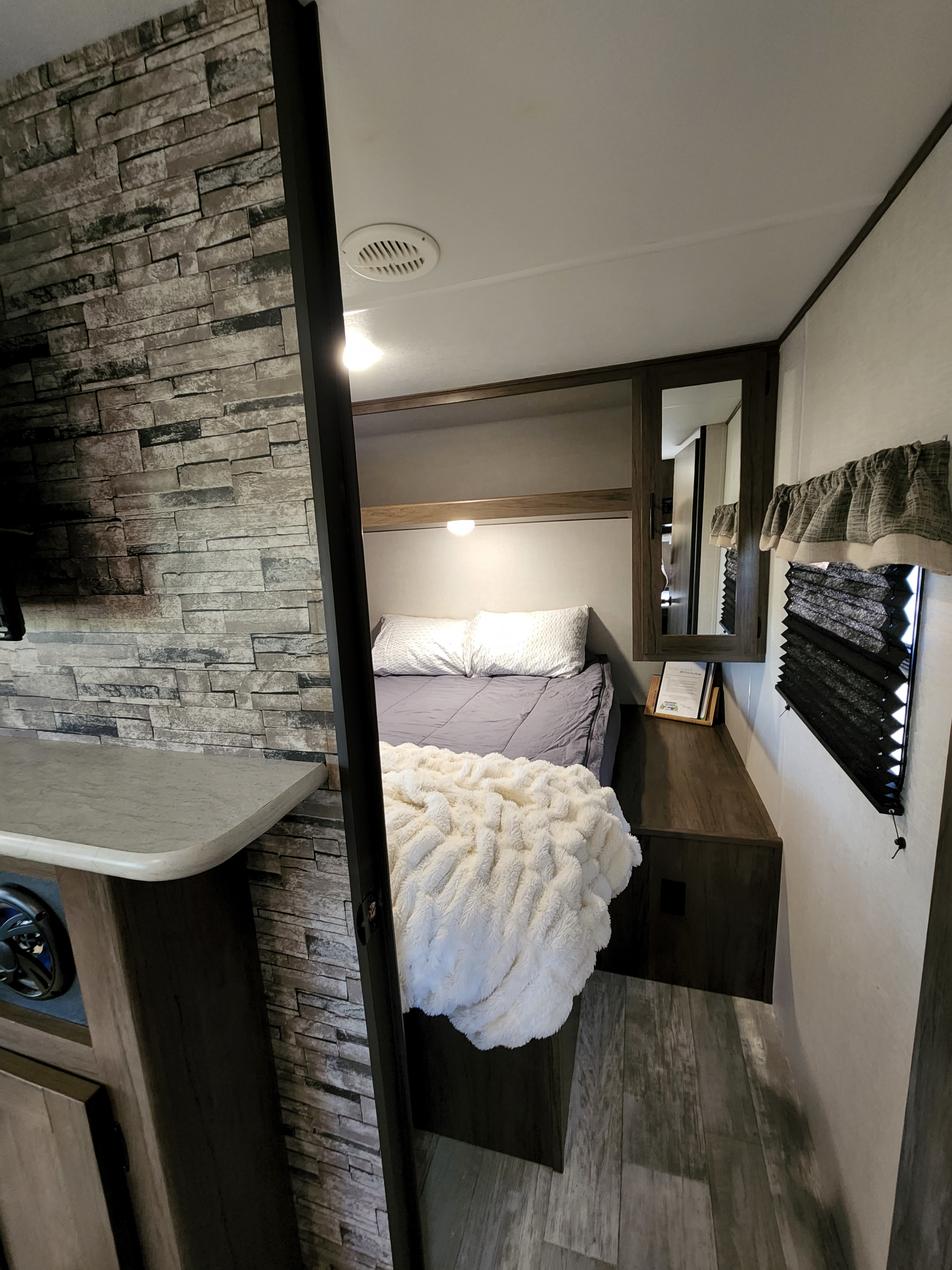 RV rental interior: A comfortable and modern bedroom area with a plush bed, stone accent wall, and practical storage.. Prime Time Avenger 2021