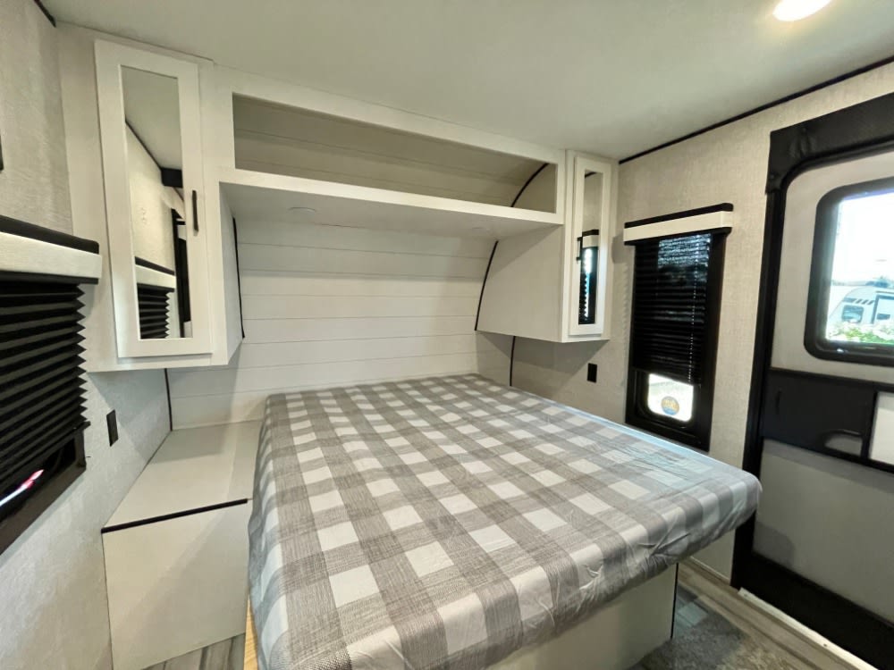 A cozy, modern RV rental bedroom with a plaid-covered bed, white cabinets, and a window with blinds, ready for your next adventure.. JAYCO JAY FLIGHT 286BHSW 2024