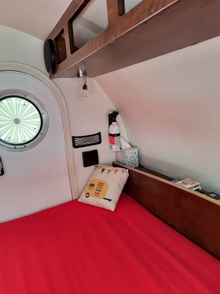 RV rental interior: A compact bedroom with a red bed, round window, and overhead storage for travel.. T@G T@G Trailer 2015